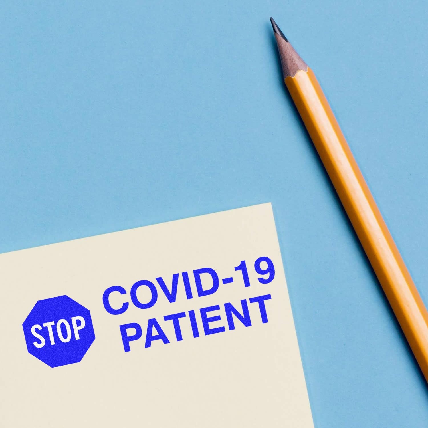 Large Self Inking Stop Covid Patient Stamp in blue ink on paper, with a yellow pencil beside it on a blue background.