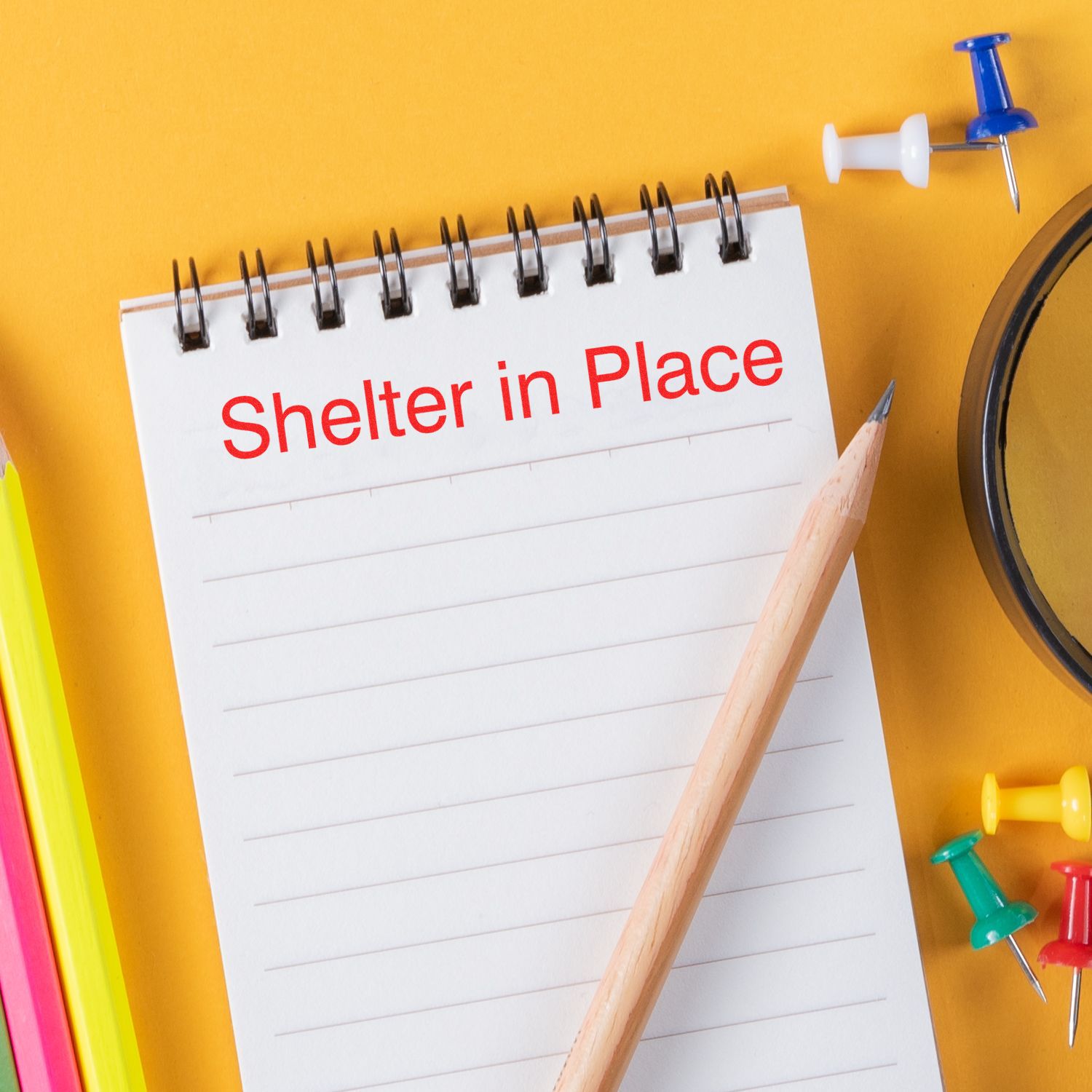 A notepad with Shelter in Place written in red, surrounded by colorful push pins and a pencil, promoting the Large Self Inking Shelter in Place Stamp.