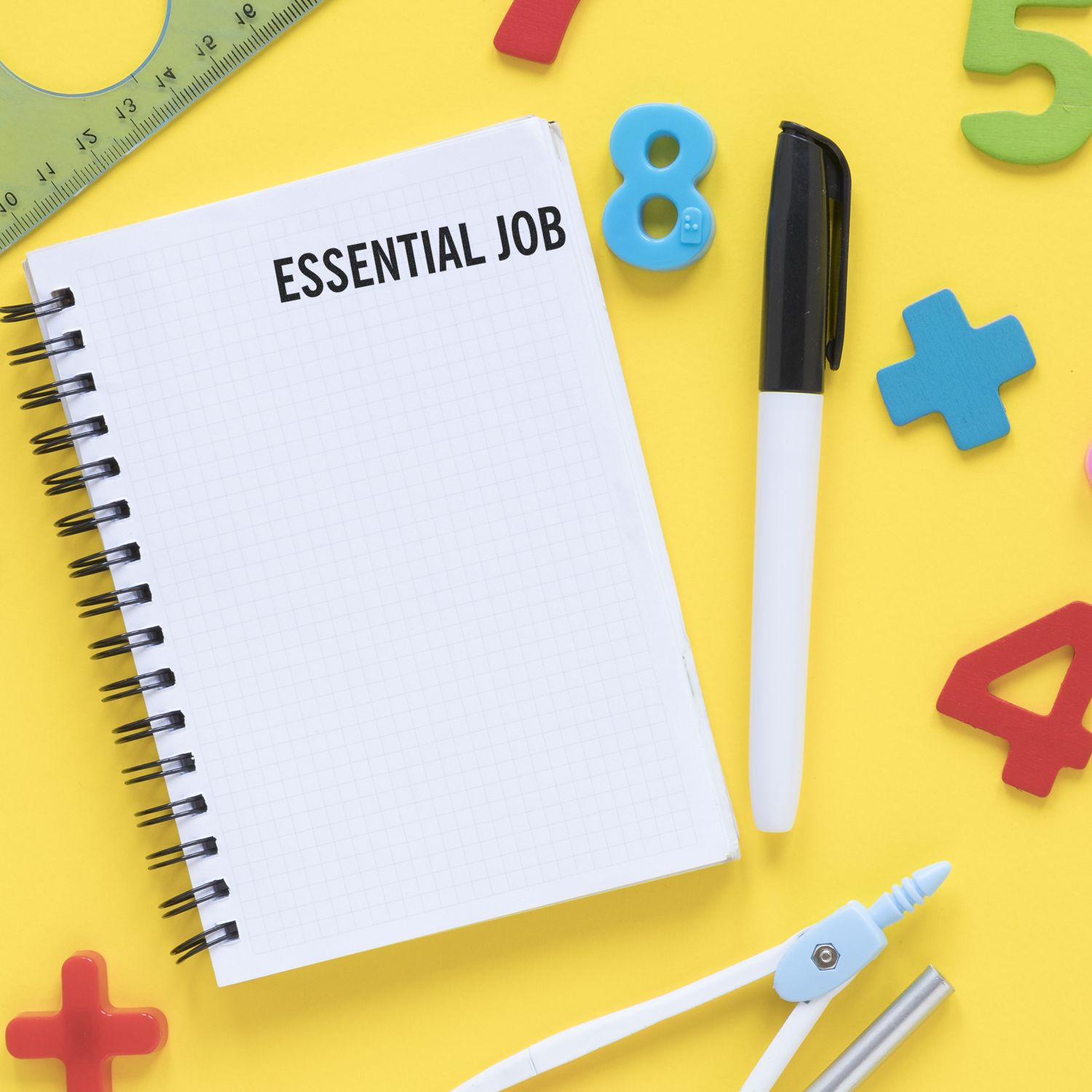 A Large Self Inking Essential Job Stamp on a notebook surrounded by a pen, ruler, and colorful numbers on a yellow background.