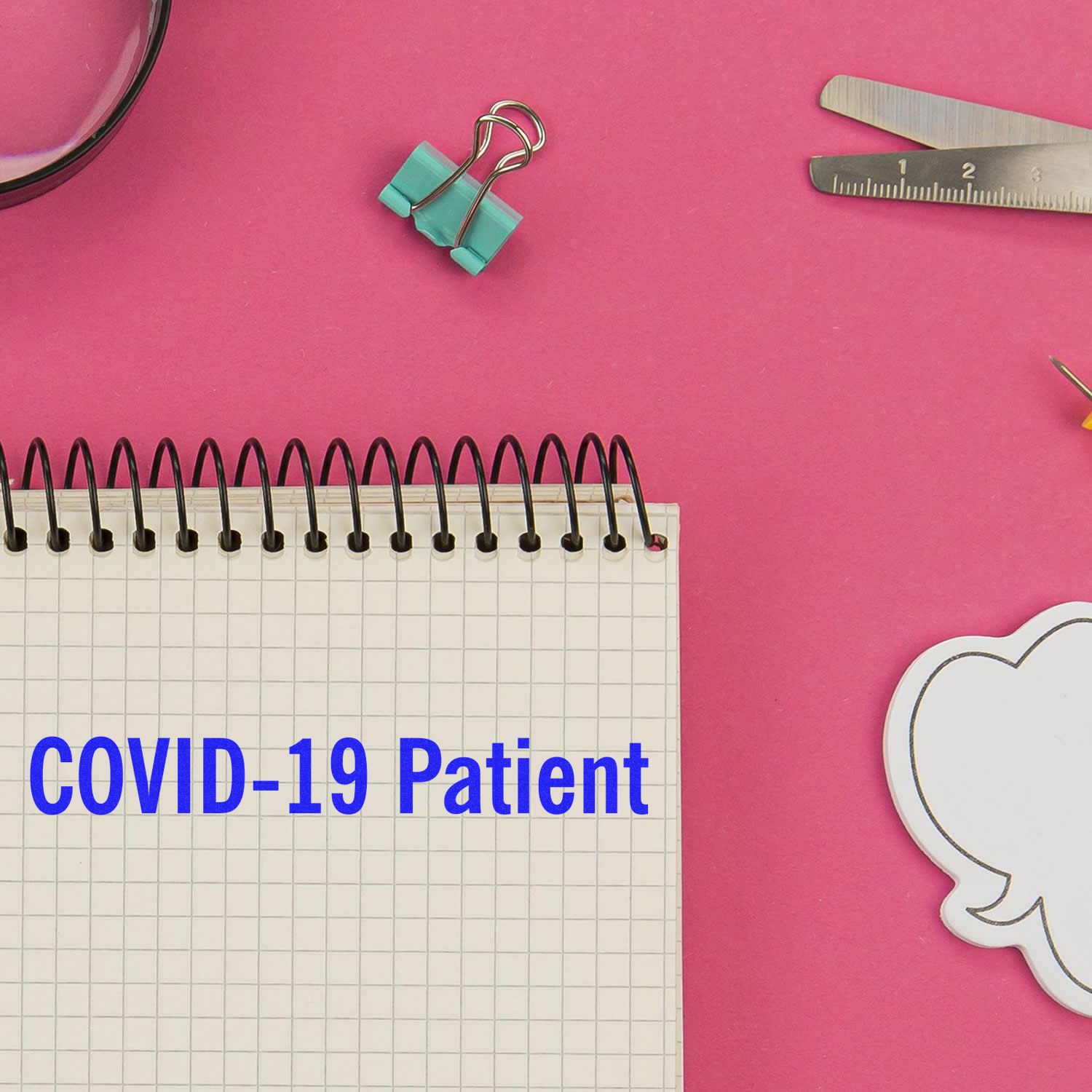 Large Self Inking Covid-19 Patient Stamp on a pink desk with a notebook, binder clip, ruler, and speech bubble sticky note.