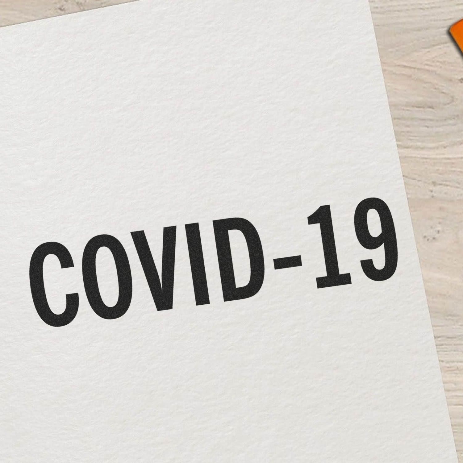 Large Self Inking Bold Covid-19 Stamp imprint on white paper, showcasing clear and bold black text reading COVID-19 on a light wooden surface.