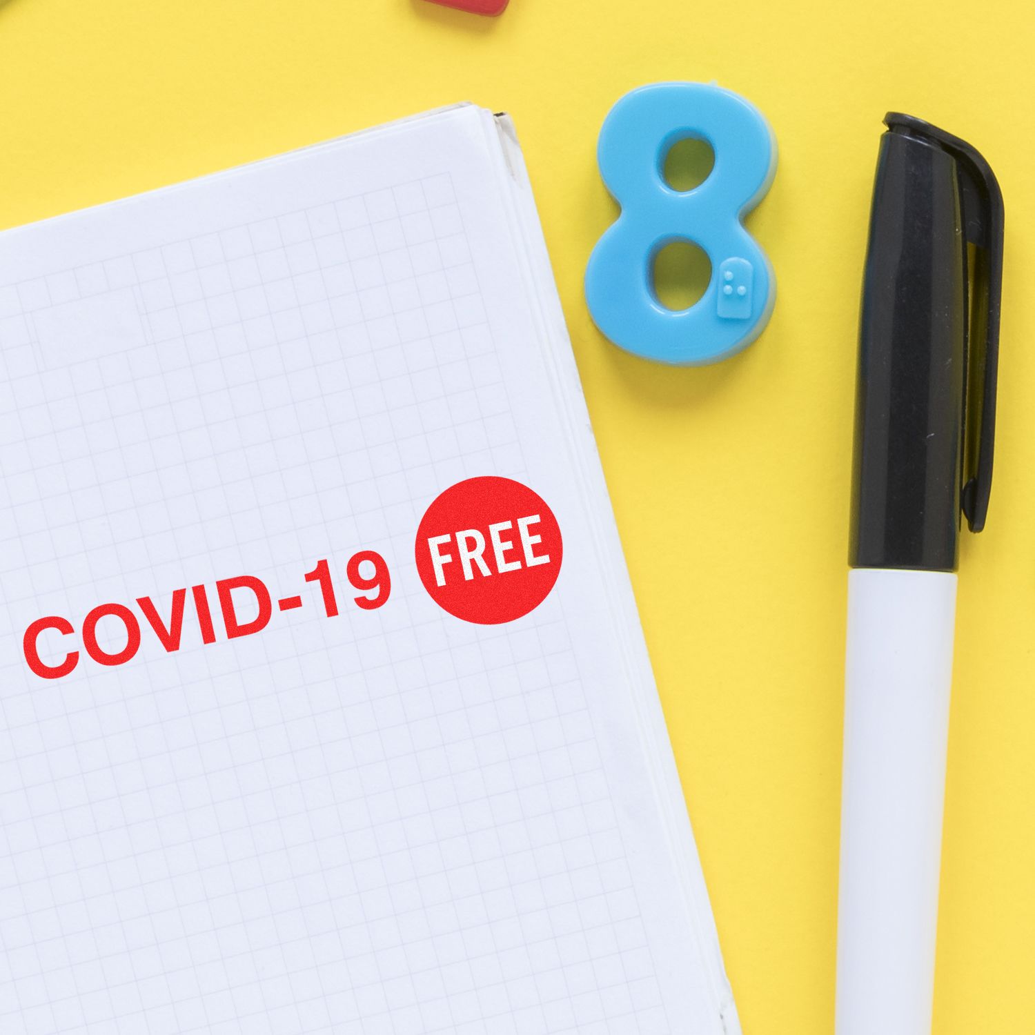 Large Self Inking Covid-19 Stamp marking COVID-19 FREE on a notebook, with a pen and a blue number 8 on a yellow background.