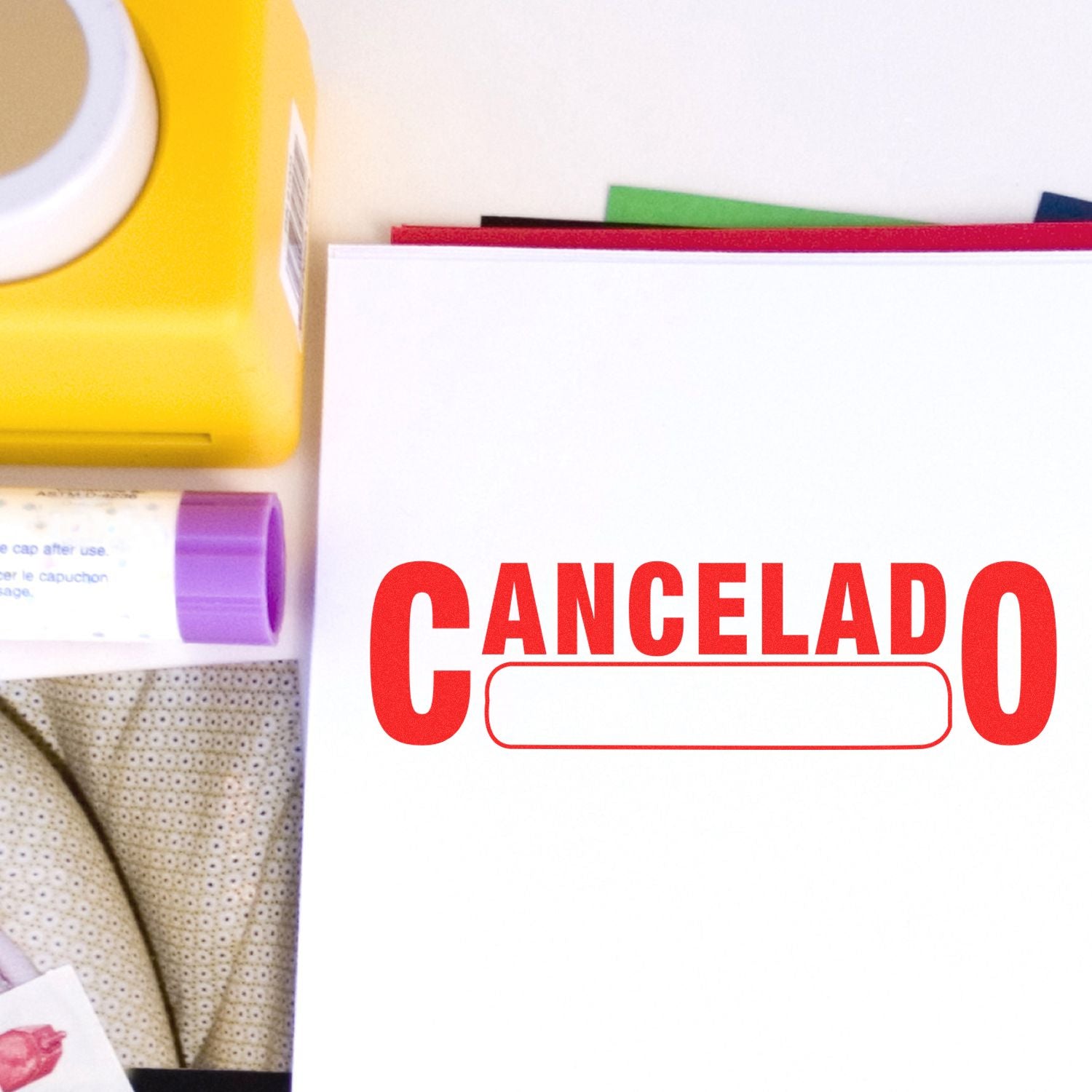 Large Self Inking Cancelado with Box Stamp in red ink on white paper, surrounded by office supplies including a yellow box and a purple glue stick.