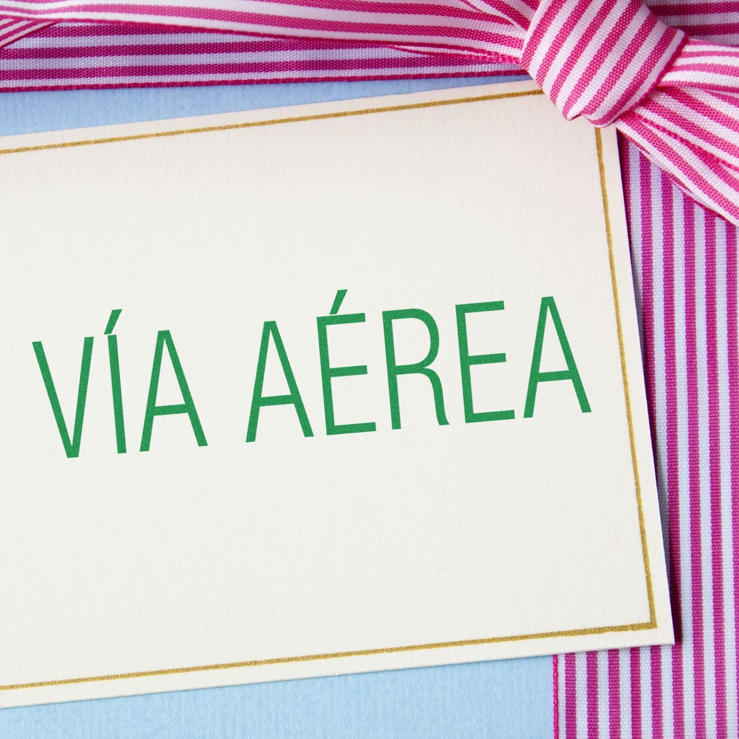 A close-up of a card with VÍA AÉREA text, tied with a pink and white striped ribbon. Product: Large Self Inking Via Aerea Stamp.