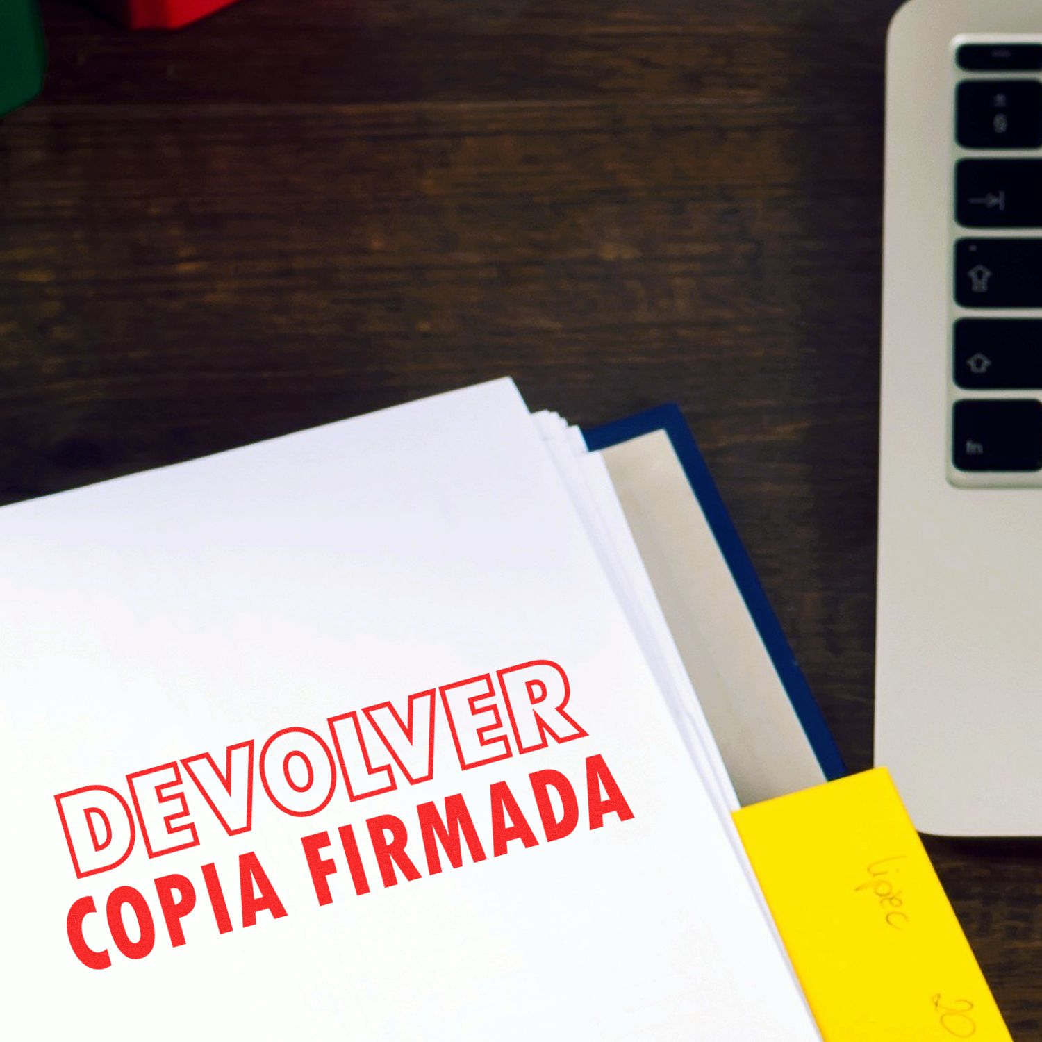 A stack of papers stamped with DEVOLVER COPIA FIRMADA using the Large Self Inking Devolver Copia Stamp, next to a laptop.