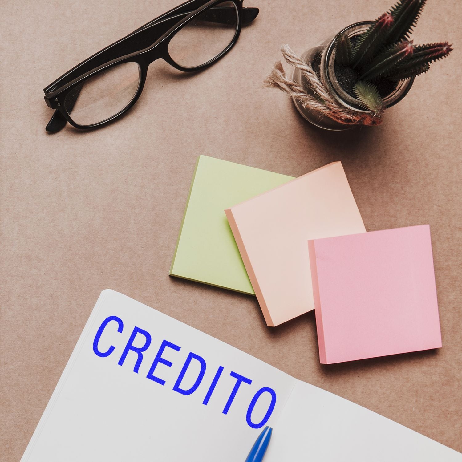 Large Self Inking Credito Stamp on a notebook, with colorful sticky notes, glasses, and a small plant on a brown desk.