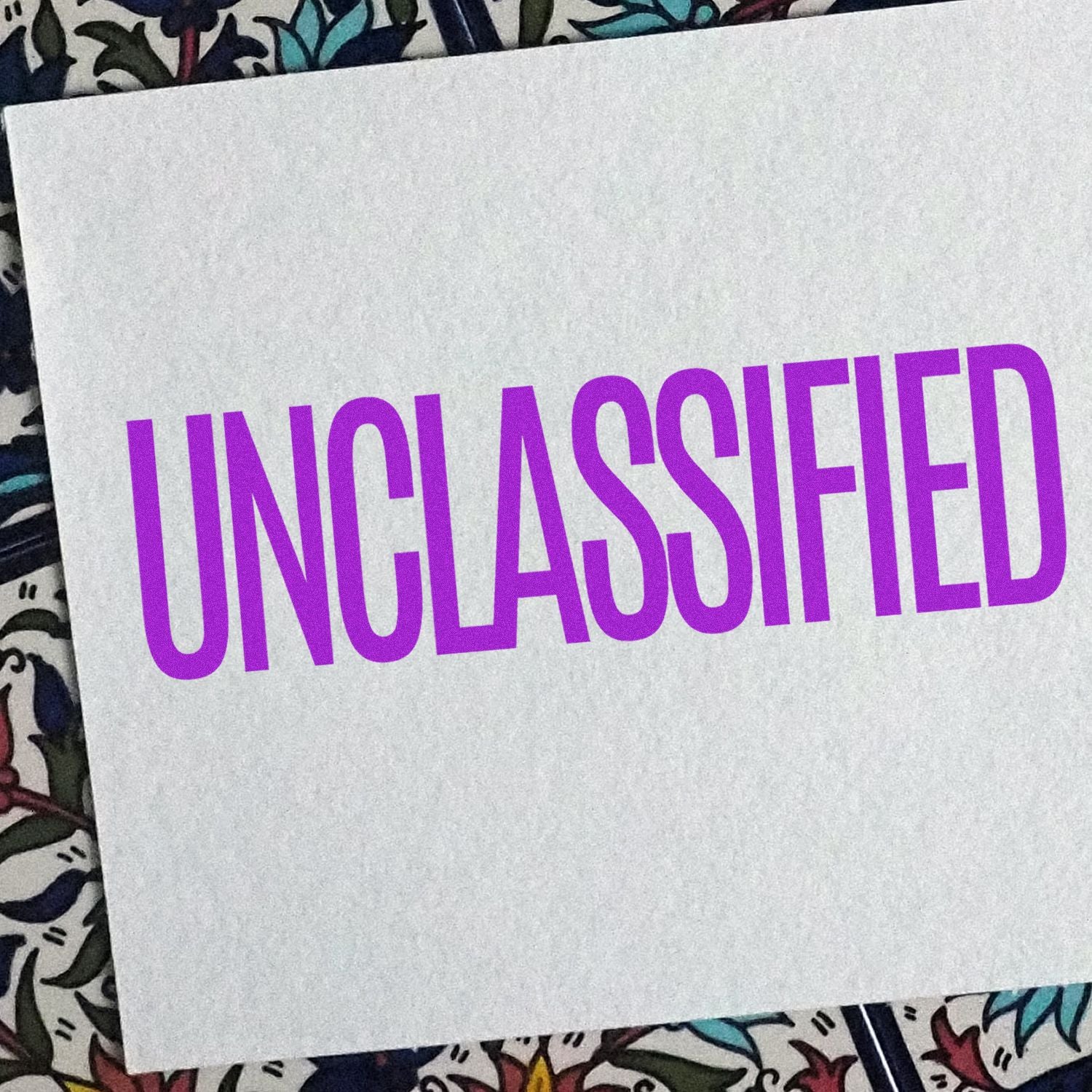 Large Pre-Inked Unclassified Stamp with bold purple UNCLASSIFIED text on a white background, placed on a patterned surface.