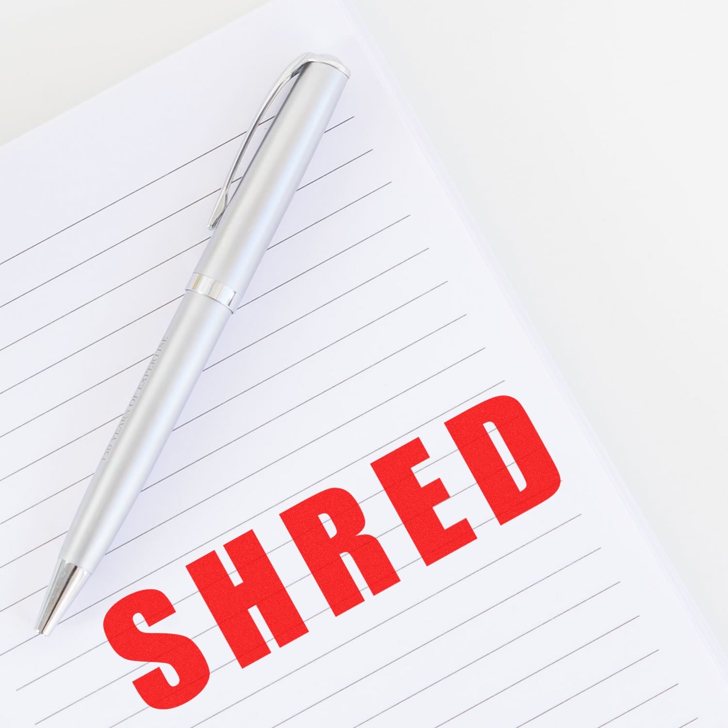 A silver pen on lined paper with the word SHRED stamped in bold red letters using the Large Pre-Inked Bold Shred Stamp.