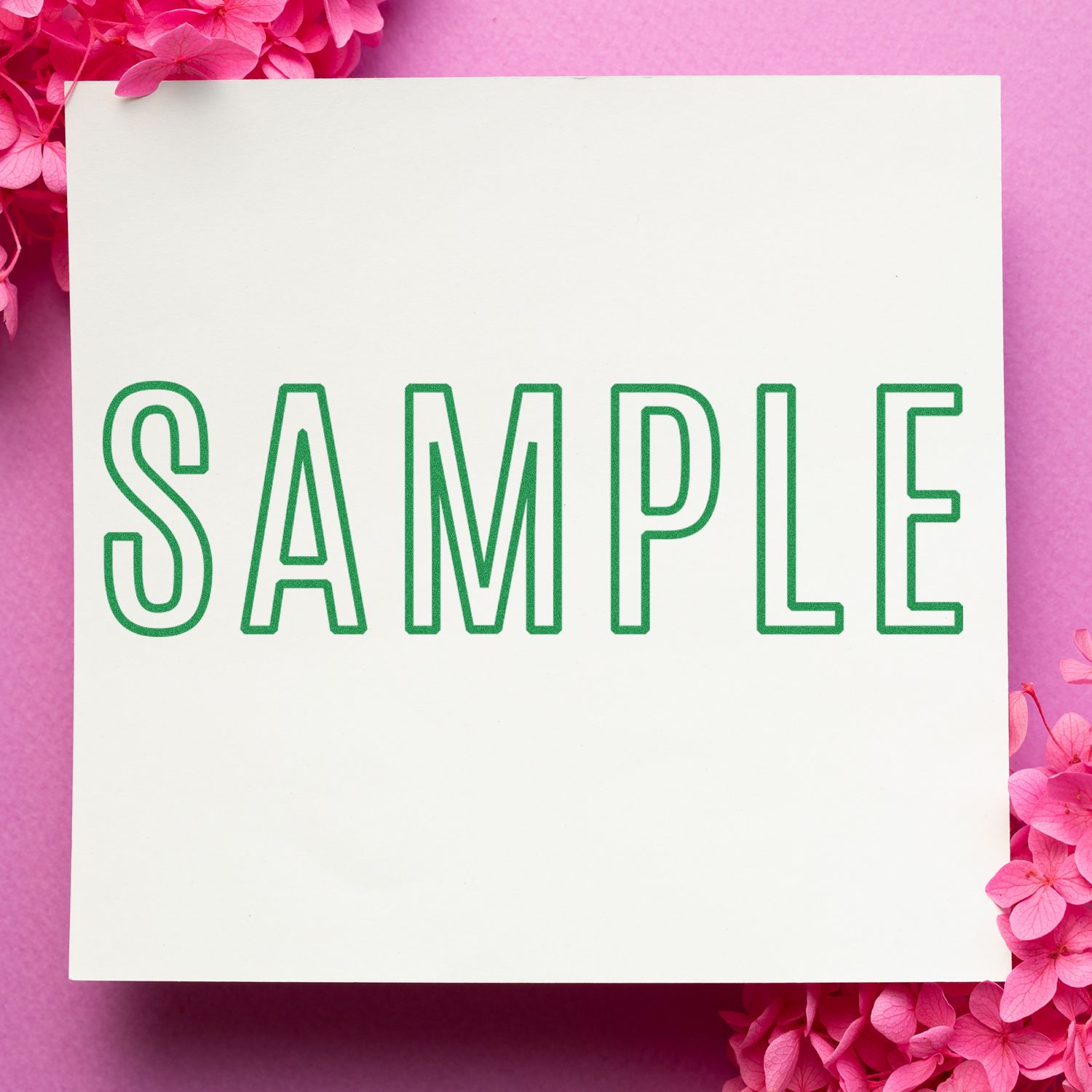 Large Pre-Inked Outline Sample Stamp in green ink on white paper, surrounded by pink flowers on a pink background.