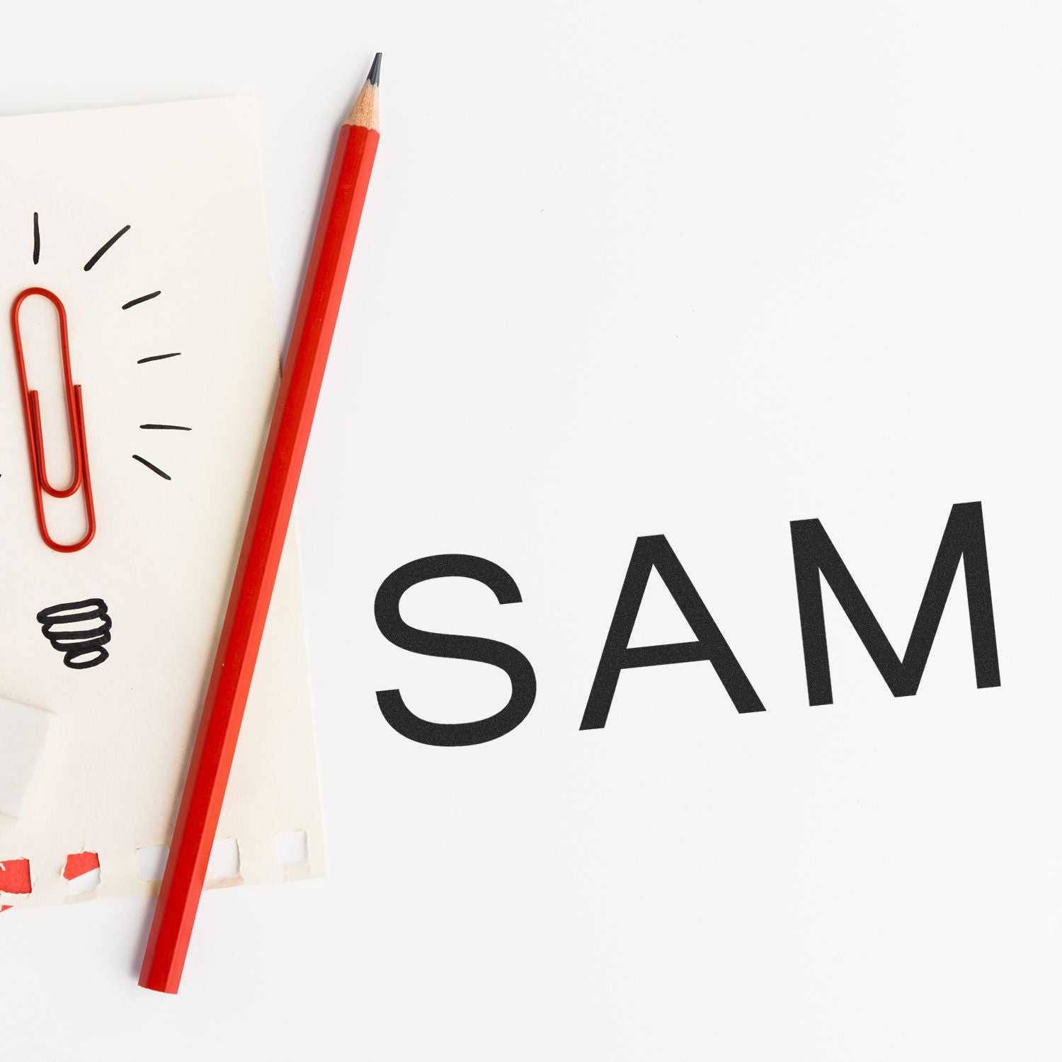 Red pencil and paperclip next to a Large Pre-Inked SAM Stamp impression on white background.