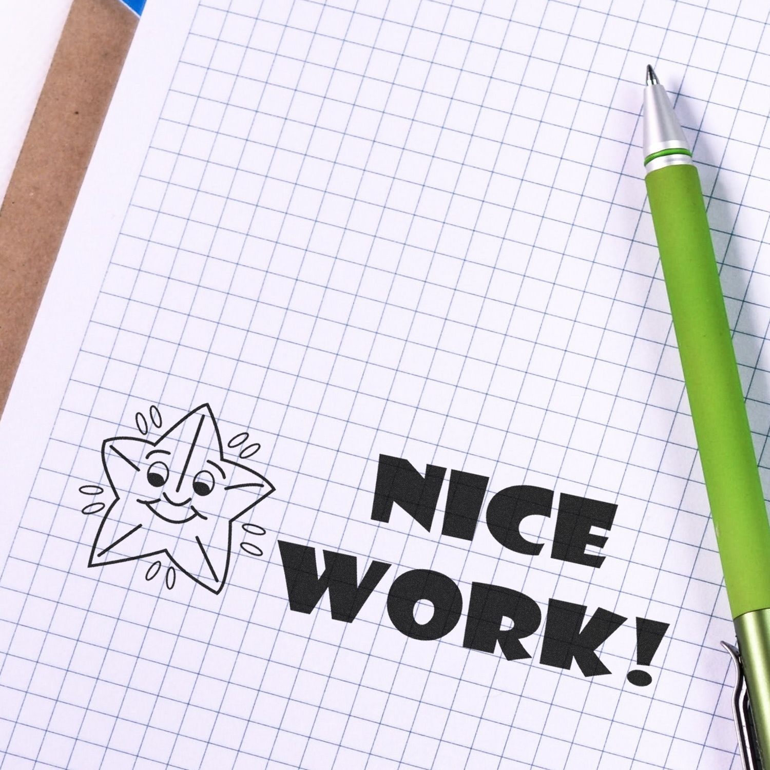 Large Pre-Inked Nice Work Stamp on graph paper with a green pen beside it, featuring a smiling star and the words NICE WORK!