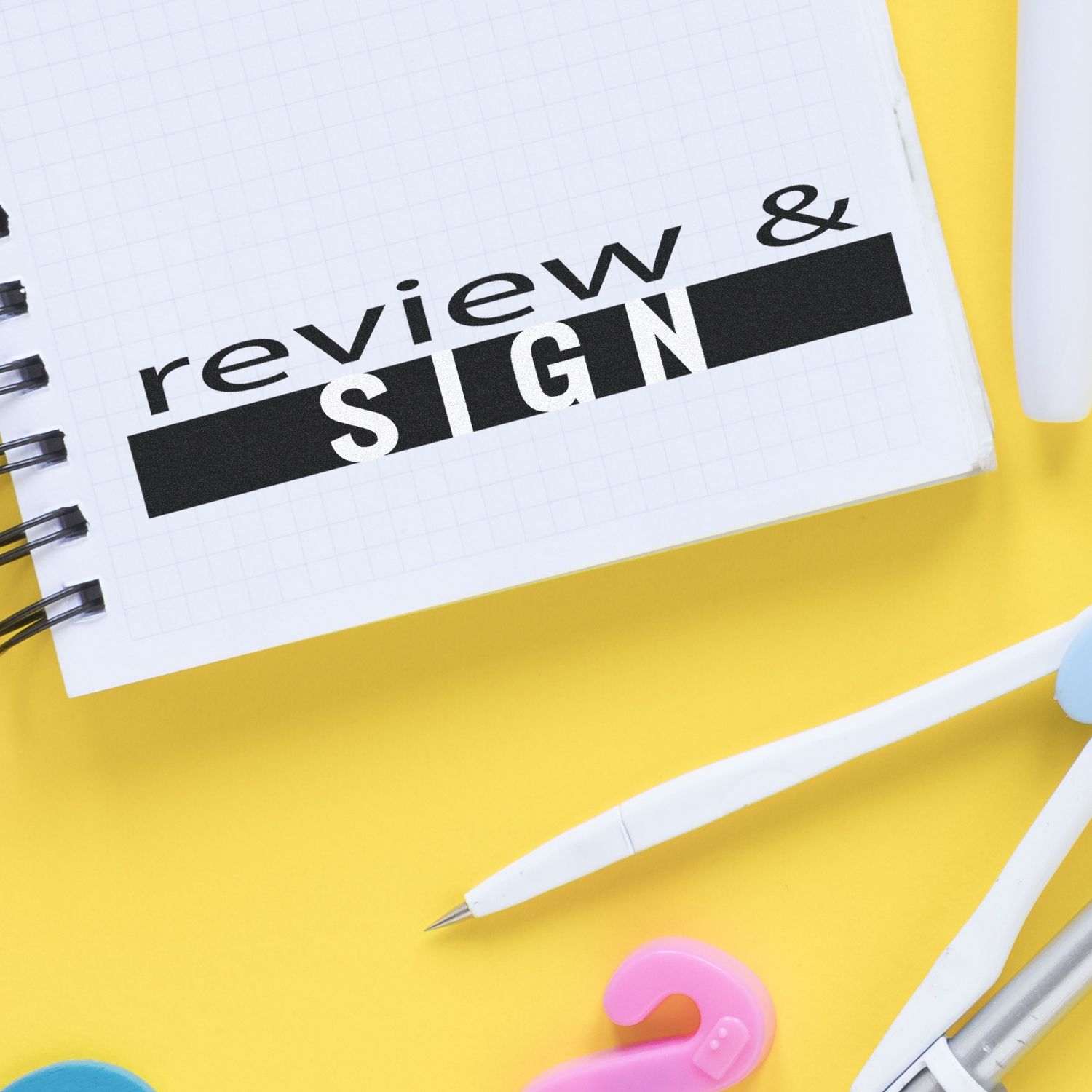 Large Pre-Inked Review and Sign Stamp on a notebook page with office supplies on a yellow background.