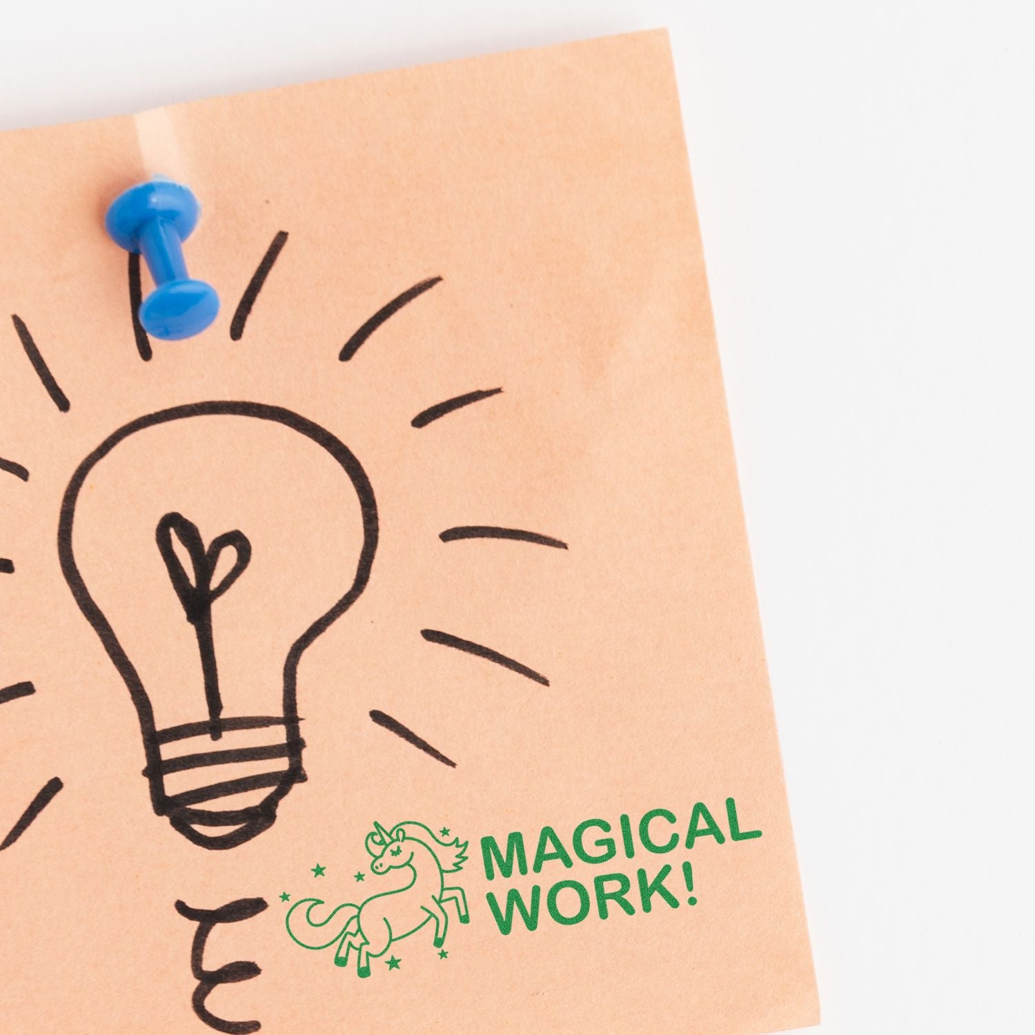 A sticky note with a lightbulb drawing pinned by a blue thumbtack, stamped with Large Pre-Inked Magical Work Stamp featuring a unicorn and stars.