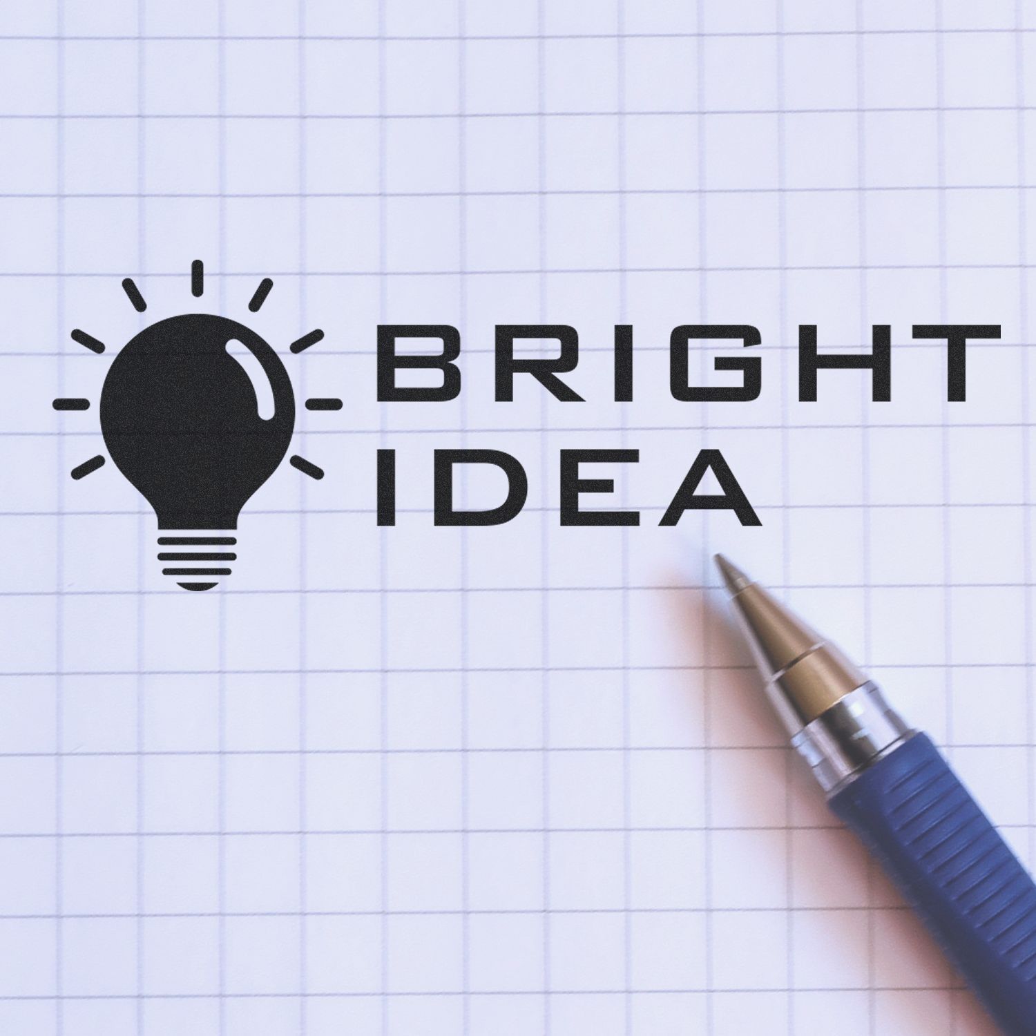 Large Pre-Inked Bright Idea Stamp imprint on graph paper with a blue pen beside it. The stamp shows a light bulb icon with the text "Bright Idea".