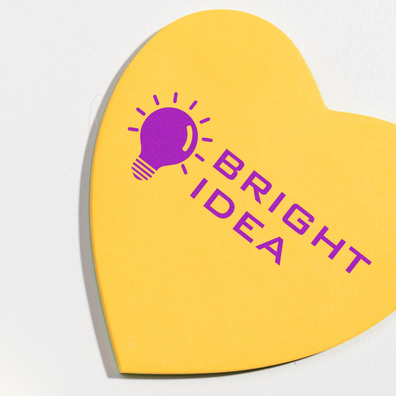 Heart-shaped yellow paper stamped with a purple light bulb and the words BRIGHT IDEA using the Large Pre-Inked Bright Idea Stamp.