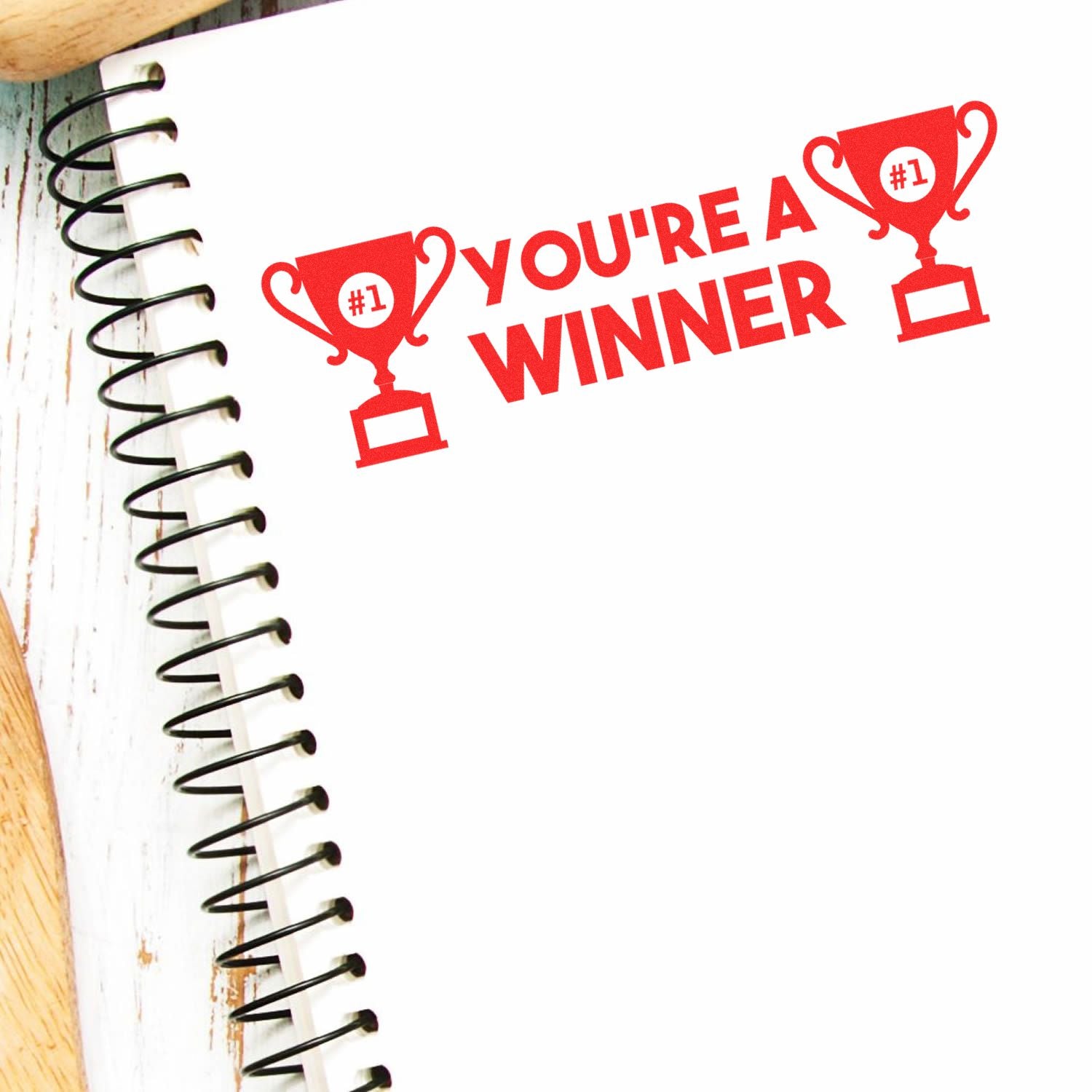 Large Pre-Inked You're a Winner Stamp in red ink on a spiral notebook, featuring two trophy icons and the text YOU'RE A WINNER.