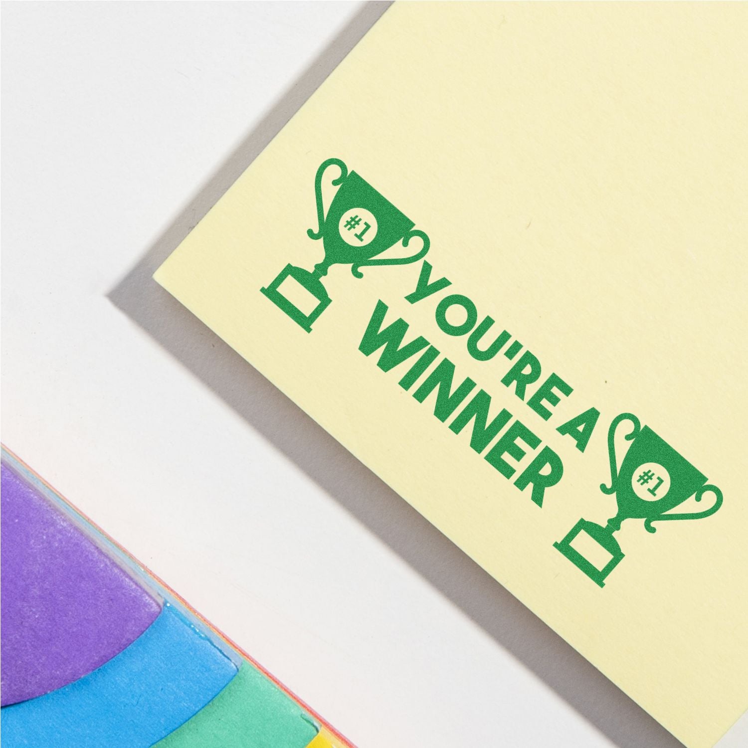 Large Pre-Inked You're a Winner Stamp in green ink on a yellow paper, featuring two trophy icons and the text YOU'RE A WINNER between them.