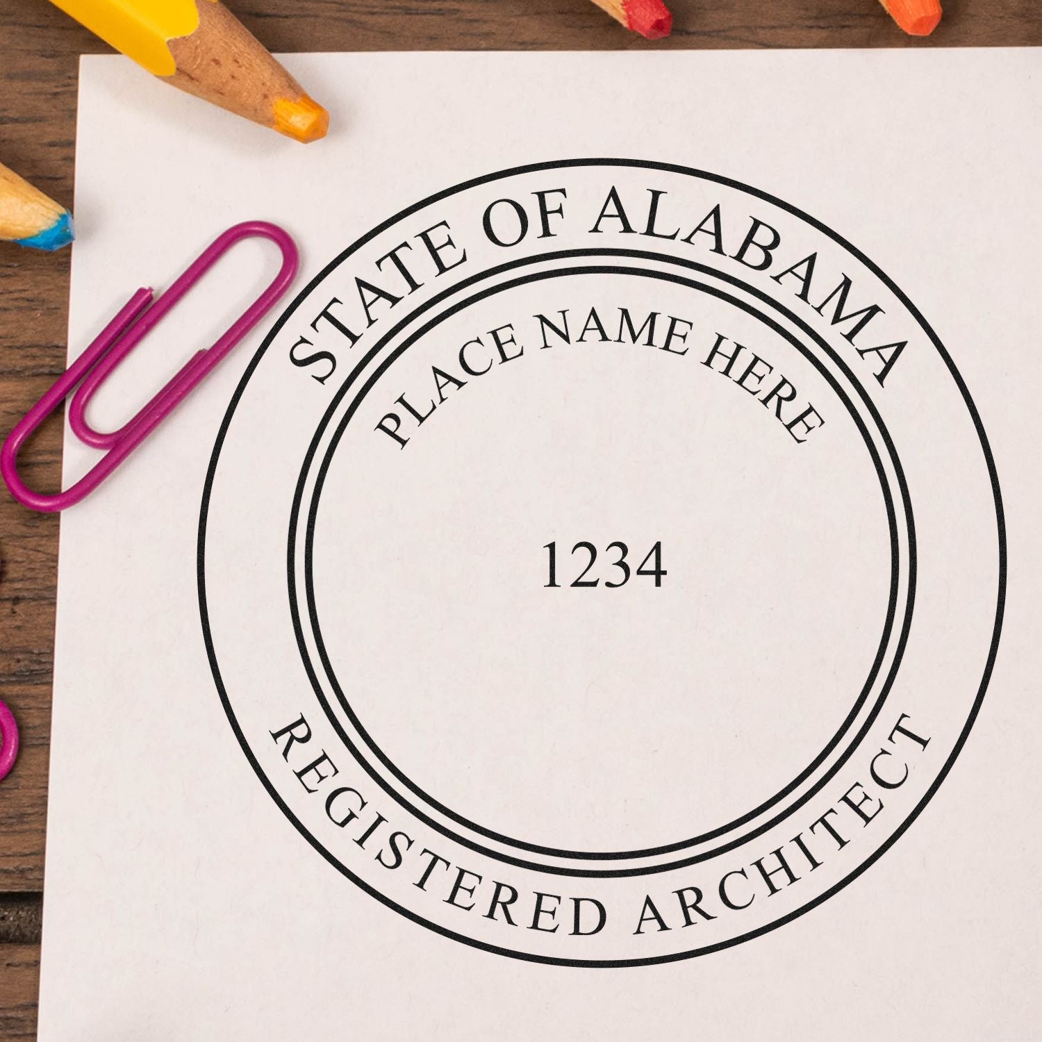 Premium MaxLight Pre-Inked Alabama Architectural Stamp on white paper with colorful paperclips and pencils in the background.