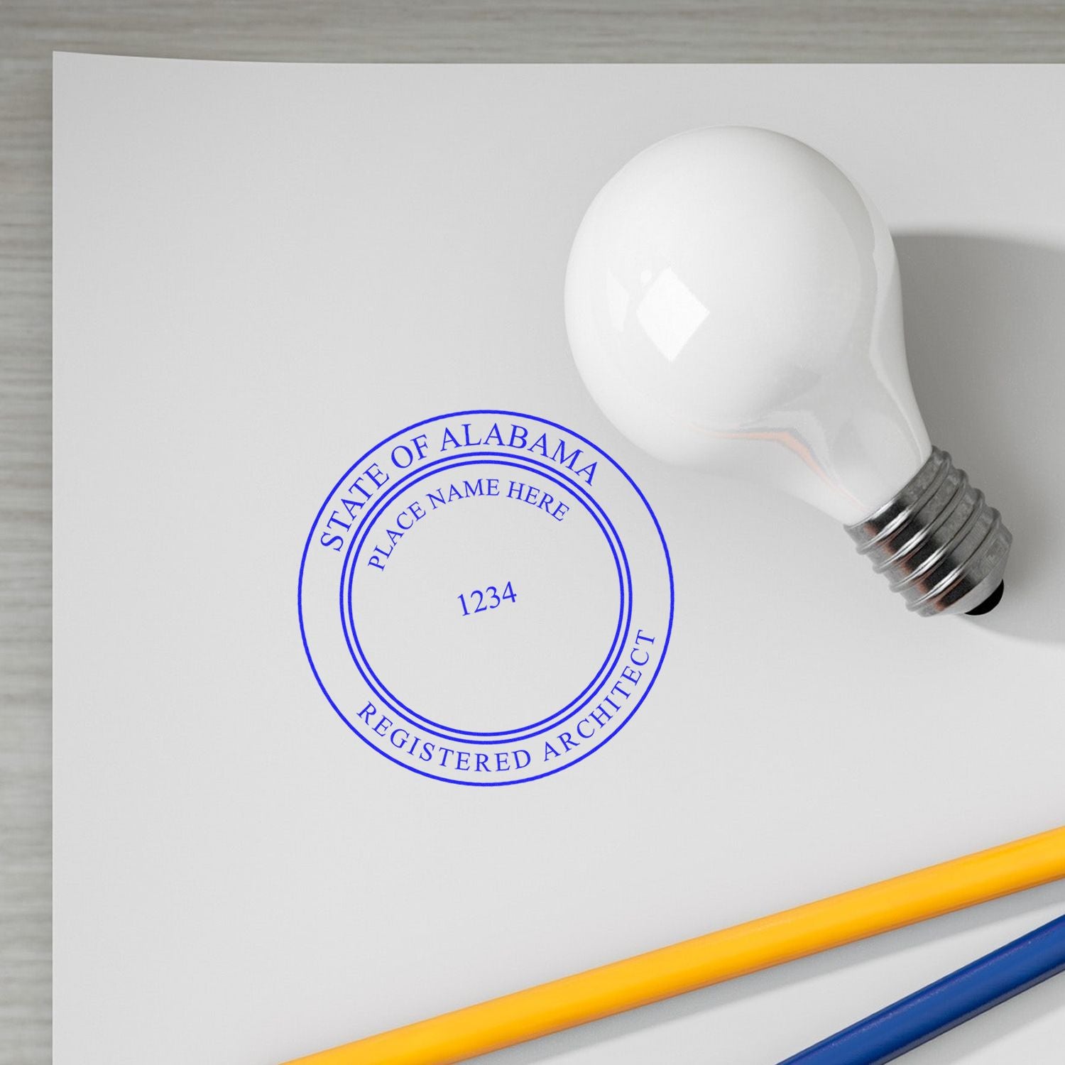 Self Inking Alabama Architect Stamp in use, showing a stamped paper with a light bulb and pencils nearby.