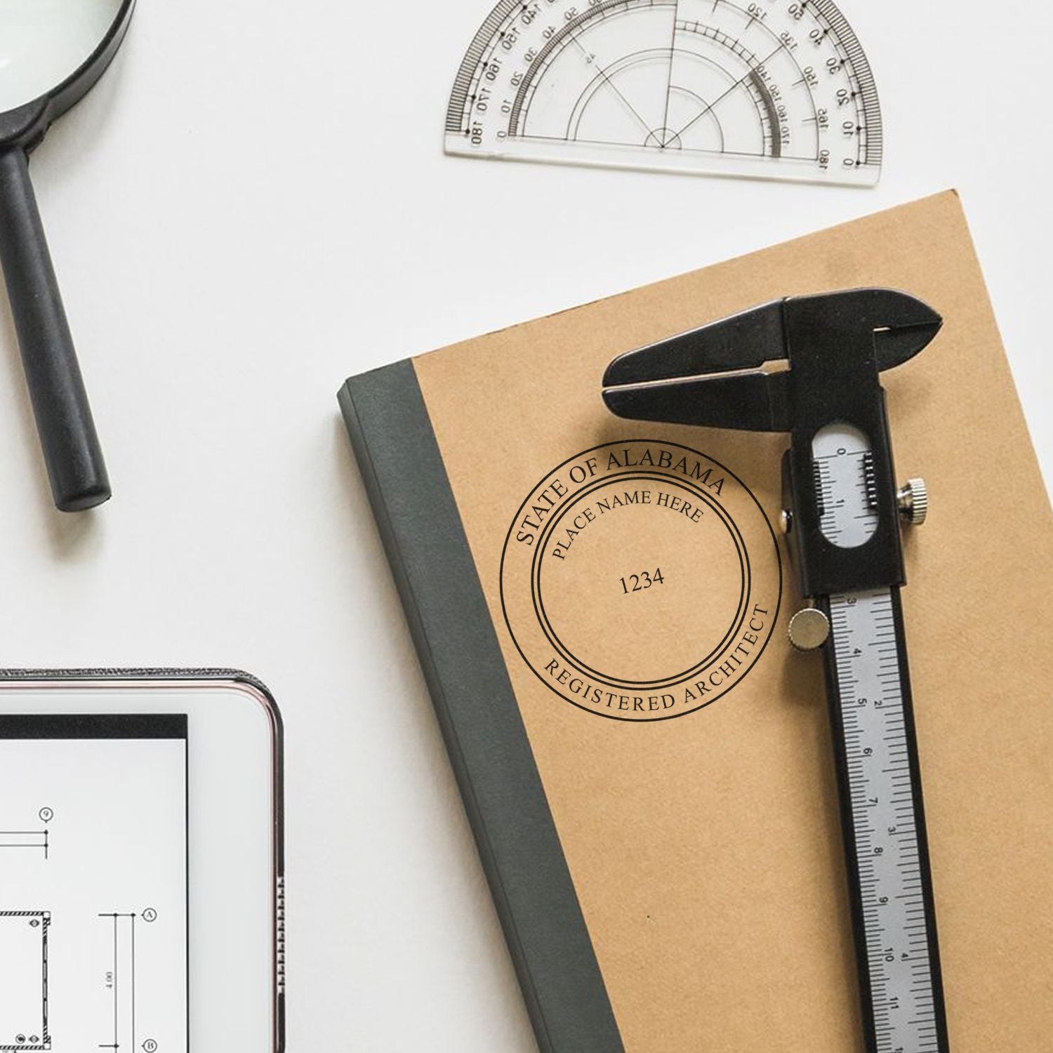 Self Inking Alabama Architect Stamp on a notebook with drafting tools, including a caliper, magnifying glass, and protractor.