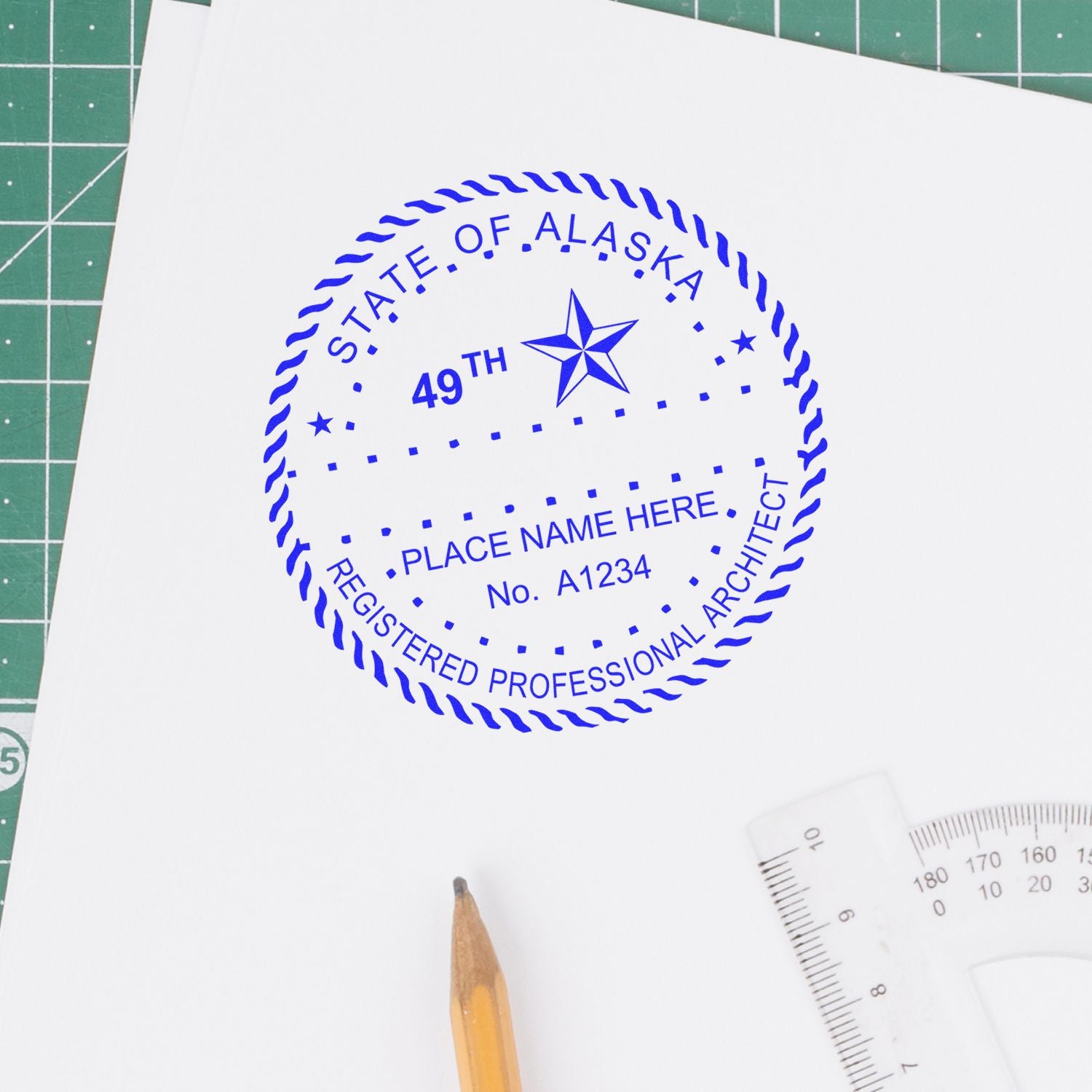 Alaska Architect Seal Stamp in blue ink on white paper, with a pencil and ruler nearby on a green cutting mat.