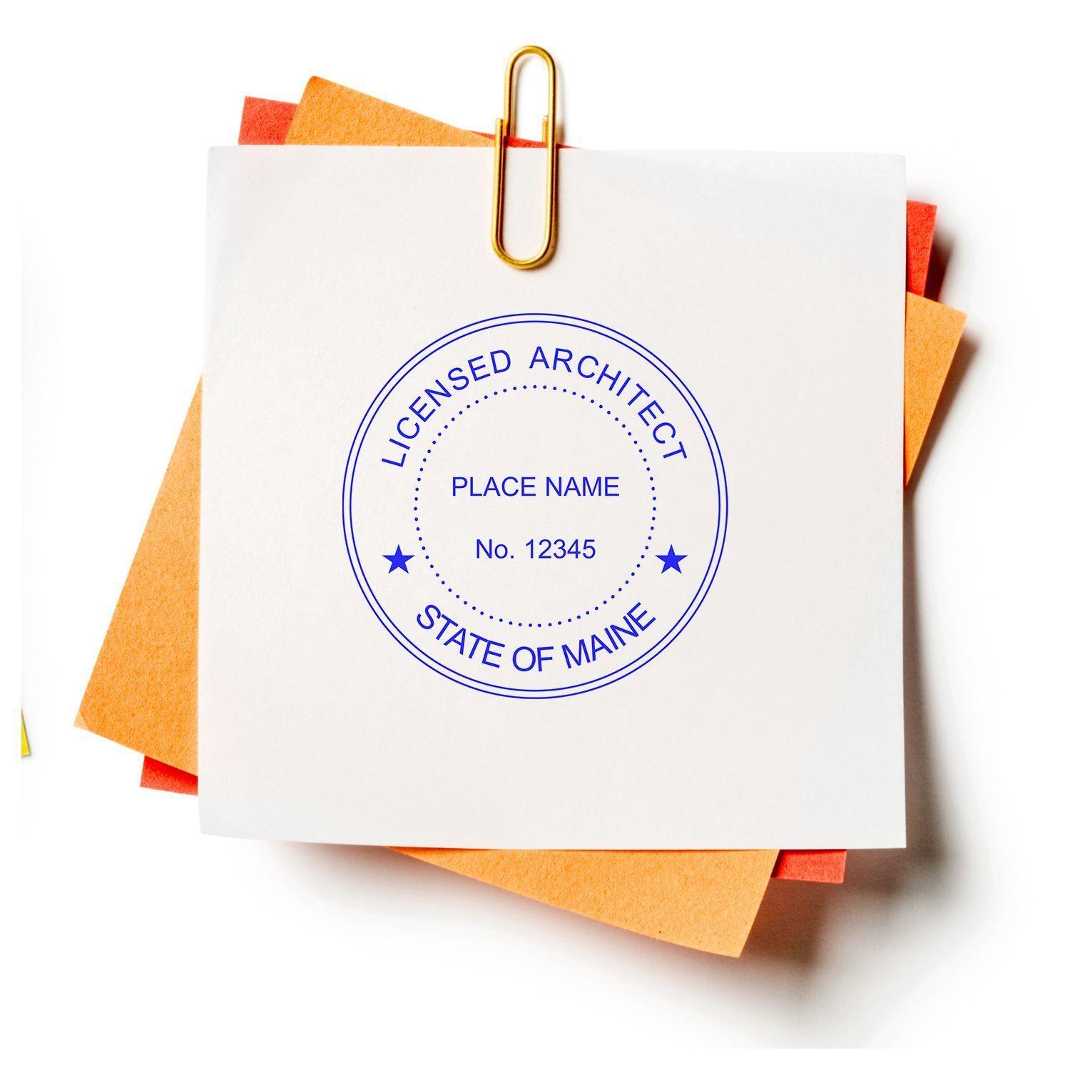 A white paper with a blue circular seal stamped using the Xstamper Architect Pre-Inked Rubber Stamp of Seal, reading Licensed Architect, State of Maine, Place Name, No. 12345, clipped to orange papers.