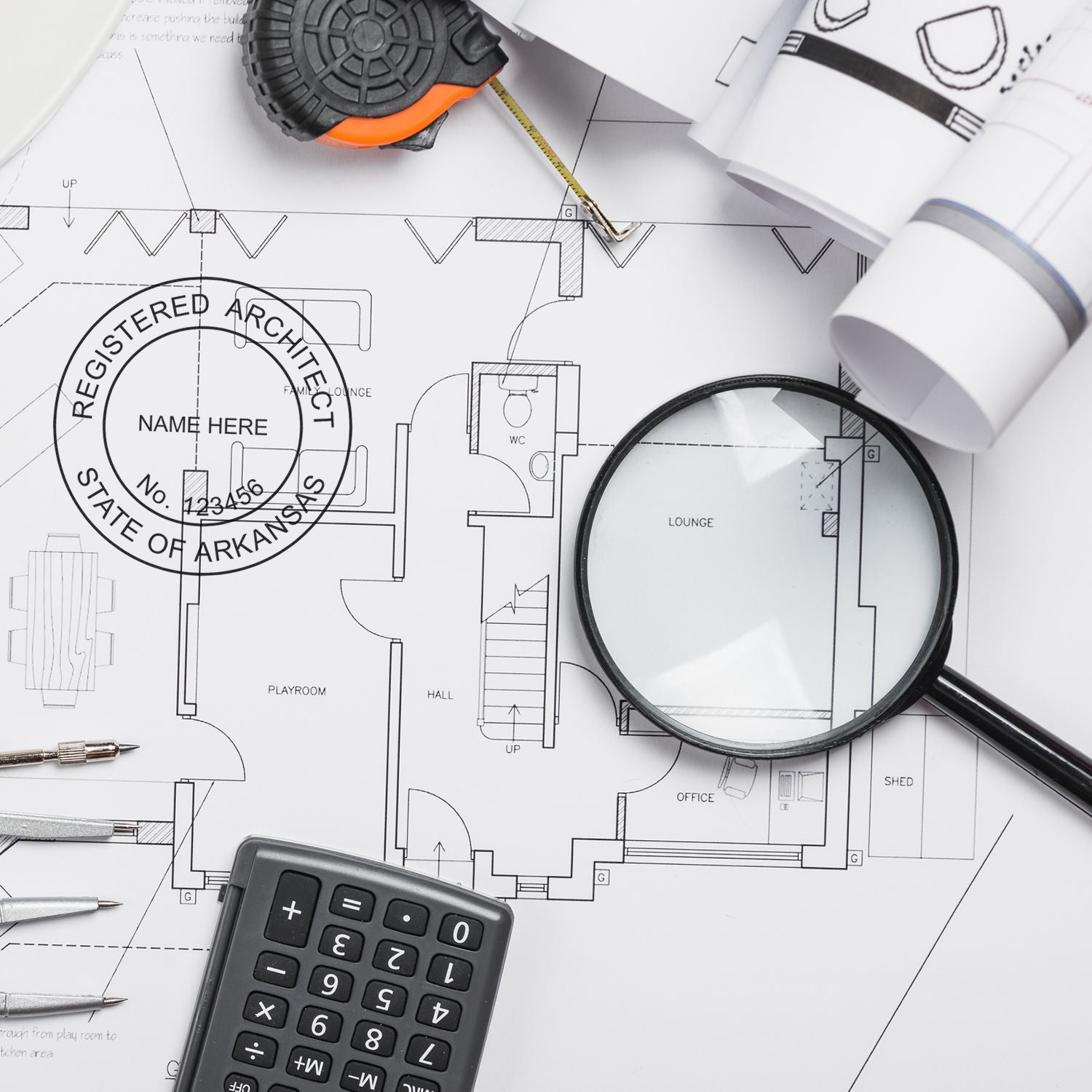 Self Inking Arkansas Architect Stamp on architectural blueprints with a magnifying glass, calculator, and drafting tools.