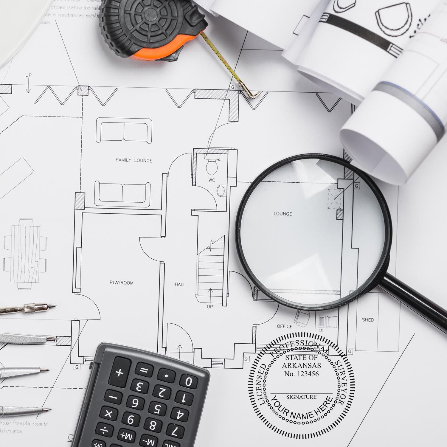 Self Inking Arkansas Land Surveyor Stamp on architectural plans with a magnifying glass, calculator, and measuring tape.