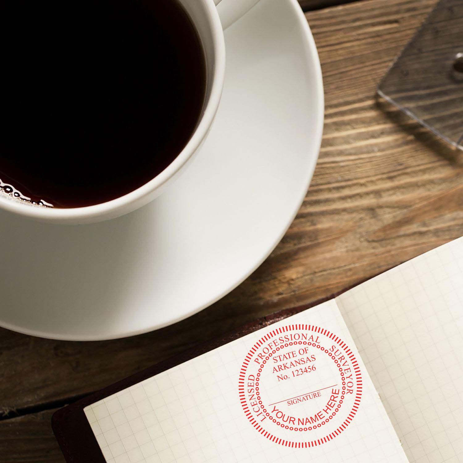 Digital Arkansas Land Surveyor Stamp, Electronic Seal for Arkansas Land Surveyor, stamped on a notebook near a cup of coffee.