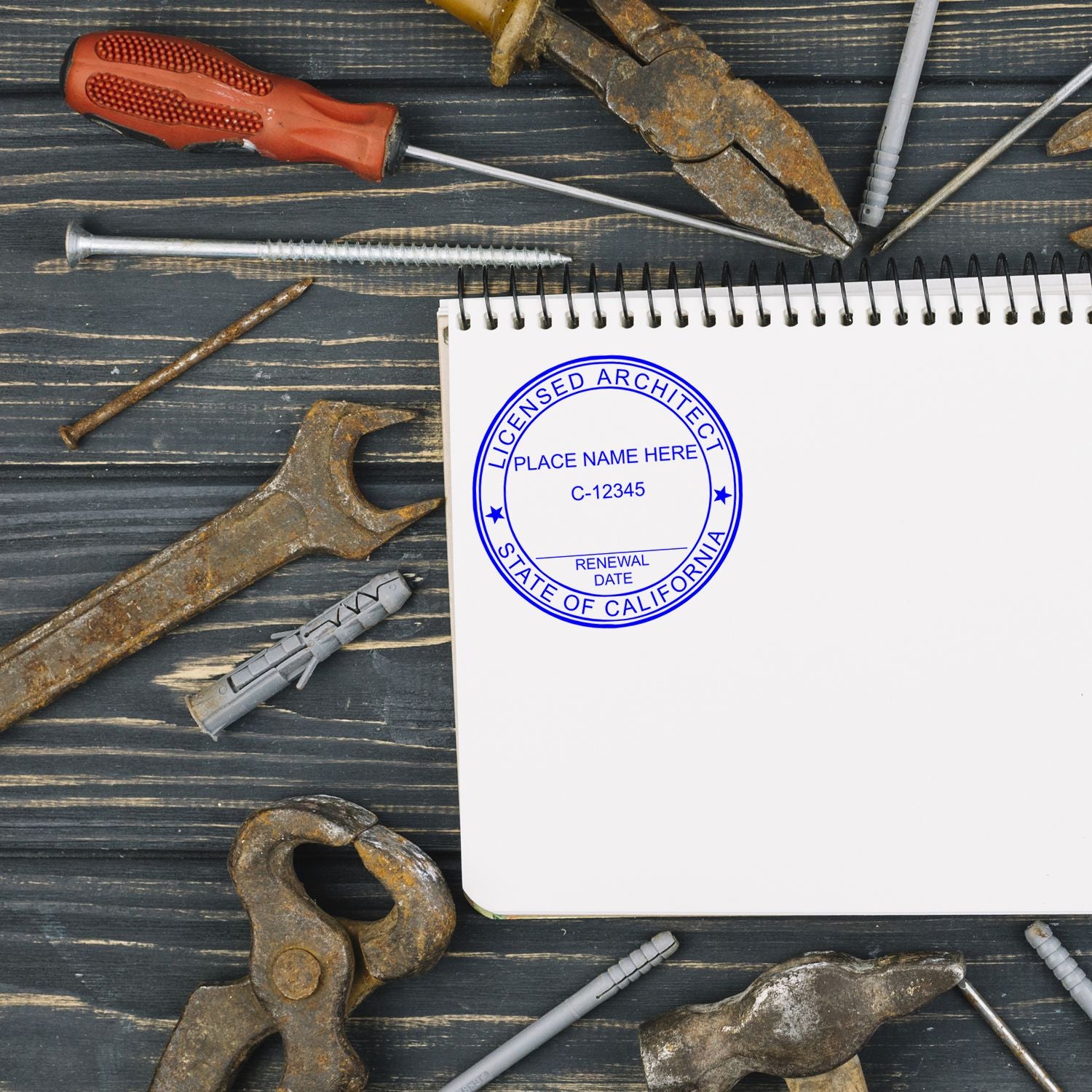 A California Architect Seal Stamp on a notepad surrounded by various tools on a wooden surface.