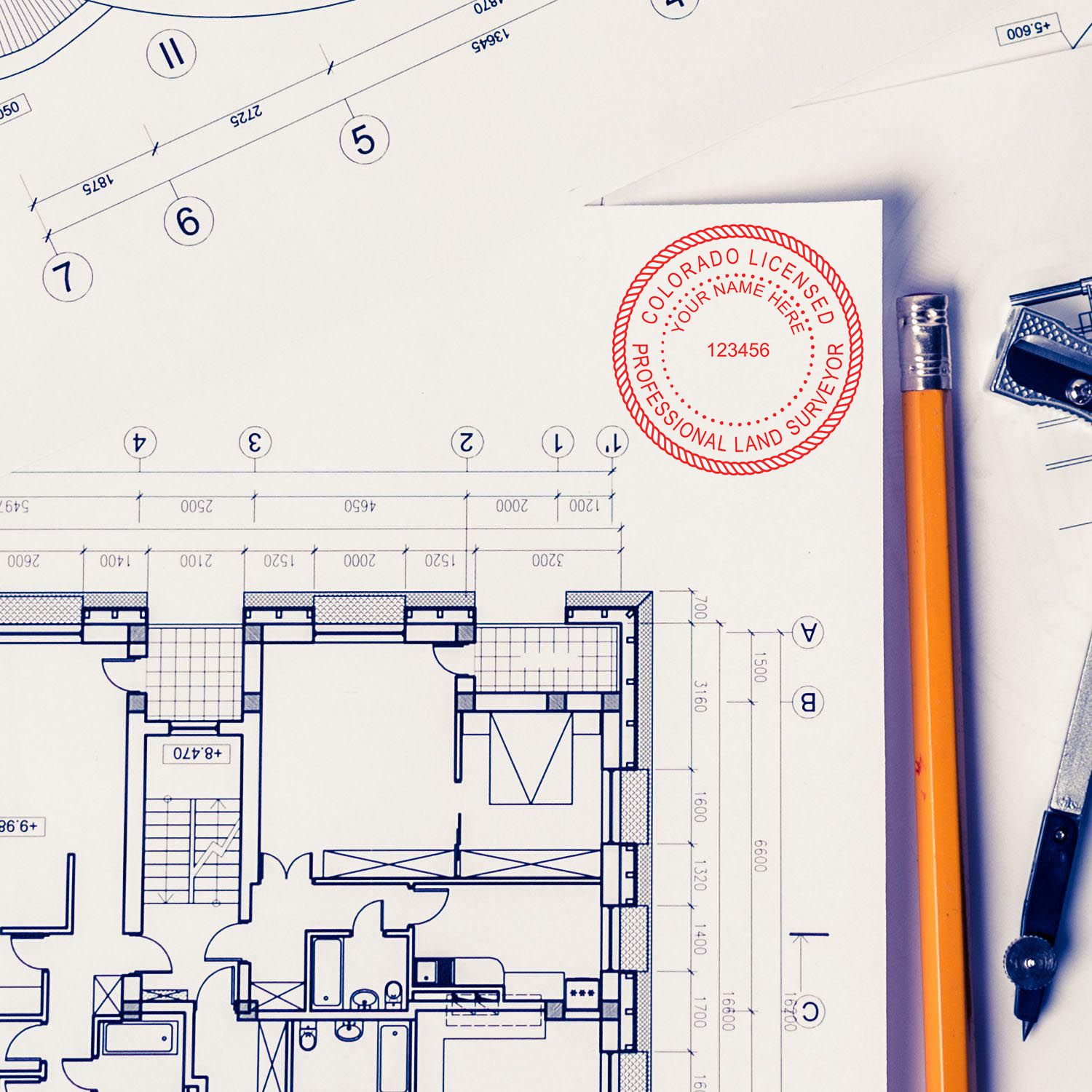Self Inking Colorado Land Surveyor Stamp on architectural blueprints with a pencil and drafting tools nearby.