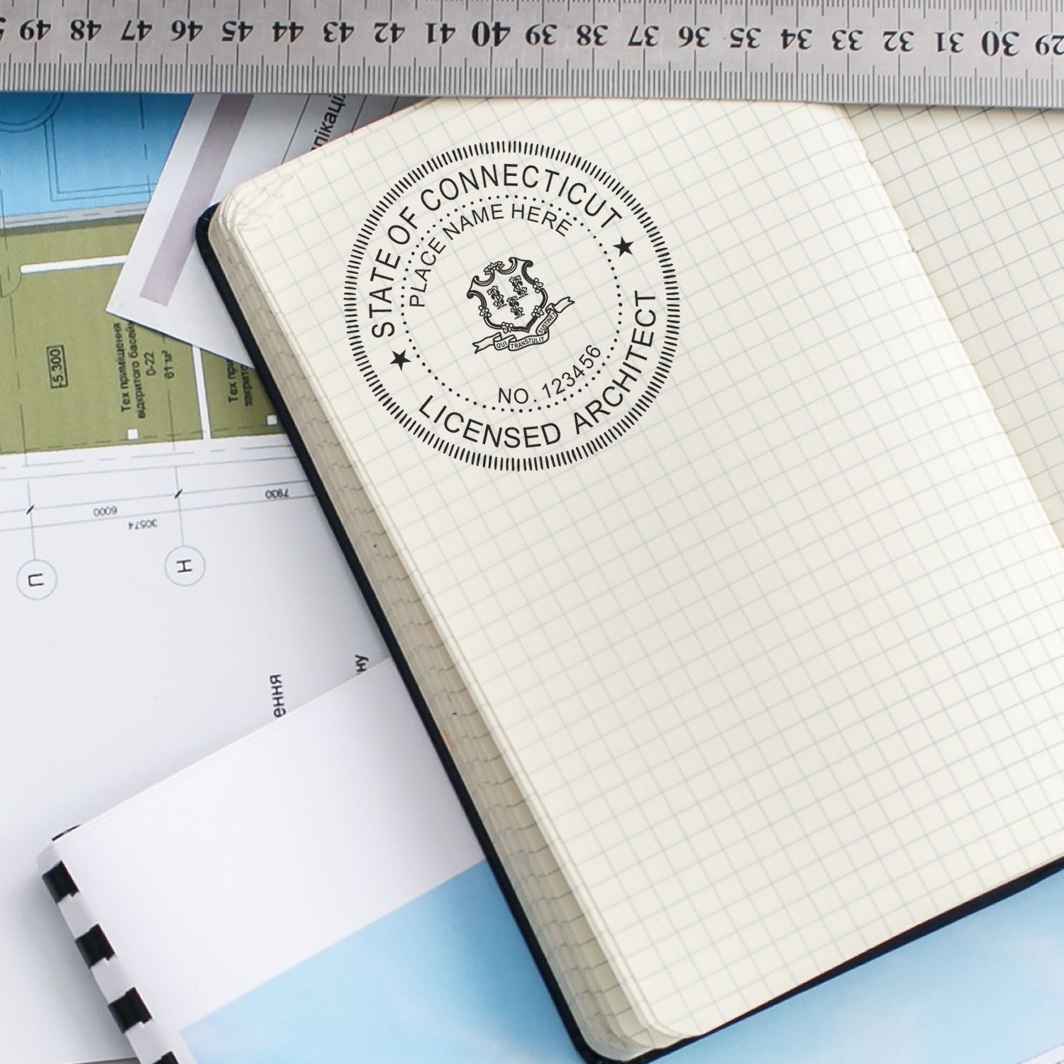 Premium MaxLight Pre-Inked Connecticut Architectural Stamp used on a grid notebook, surrounded by architectural plans and a ruler.