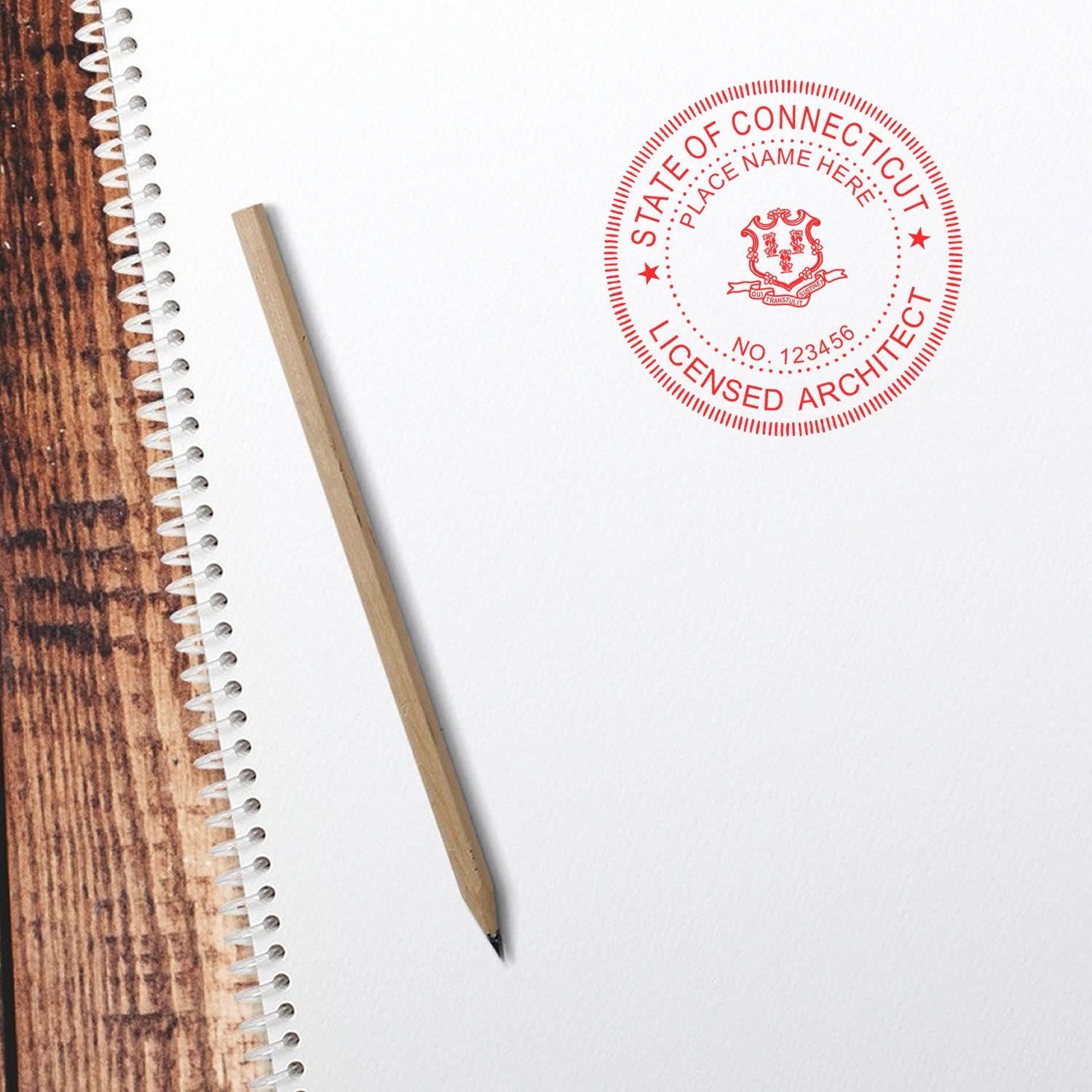 Connecticut Architect Seal Stamp in red ink on white paper, next to a pencil and spiral notebook on a wooden surface.