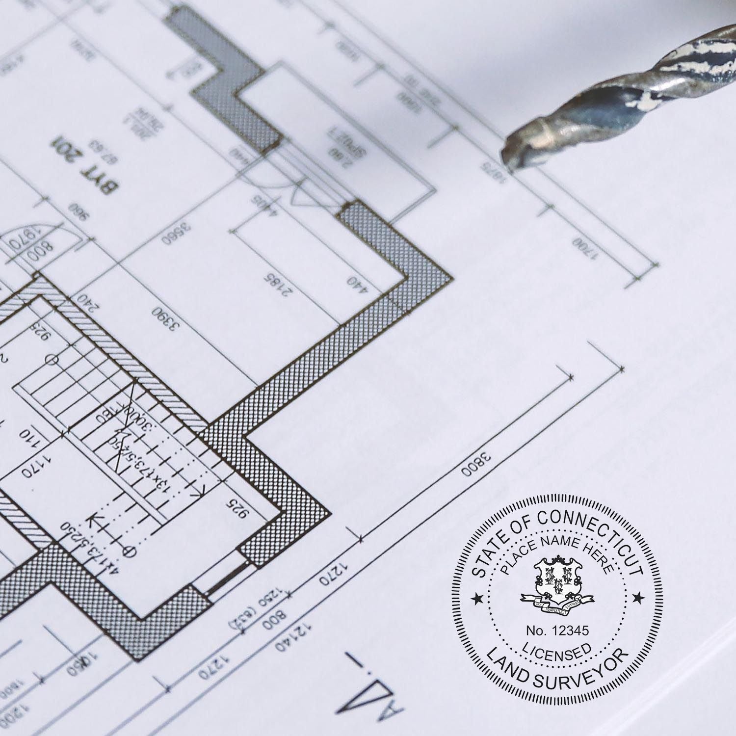 Blueprint with a Digital Connecticut Land Surveyor Stamp, Electronic Seal for Connecticut Land Surveyor, and a drill bit in the background.