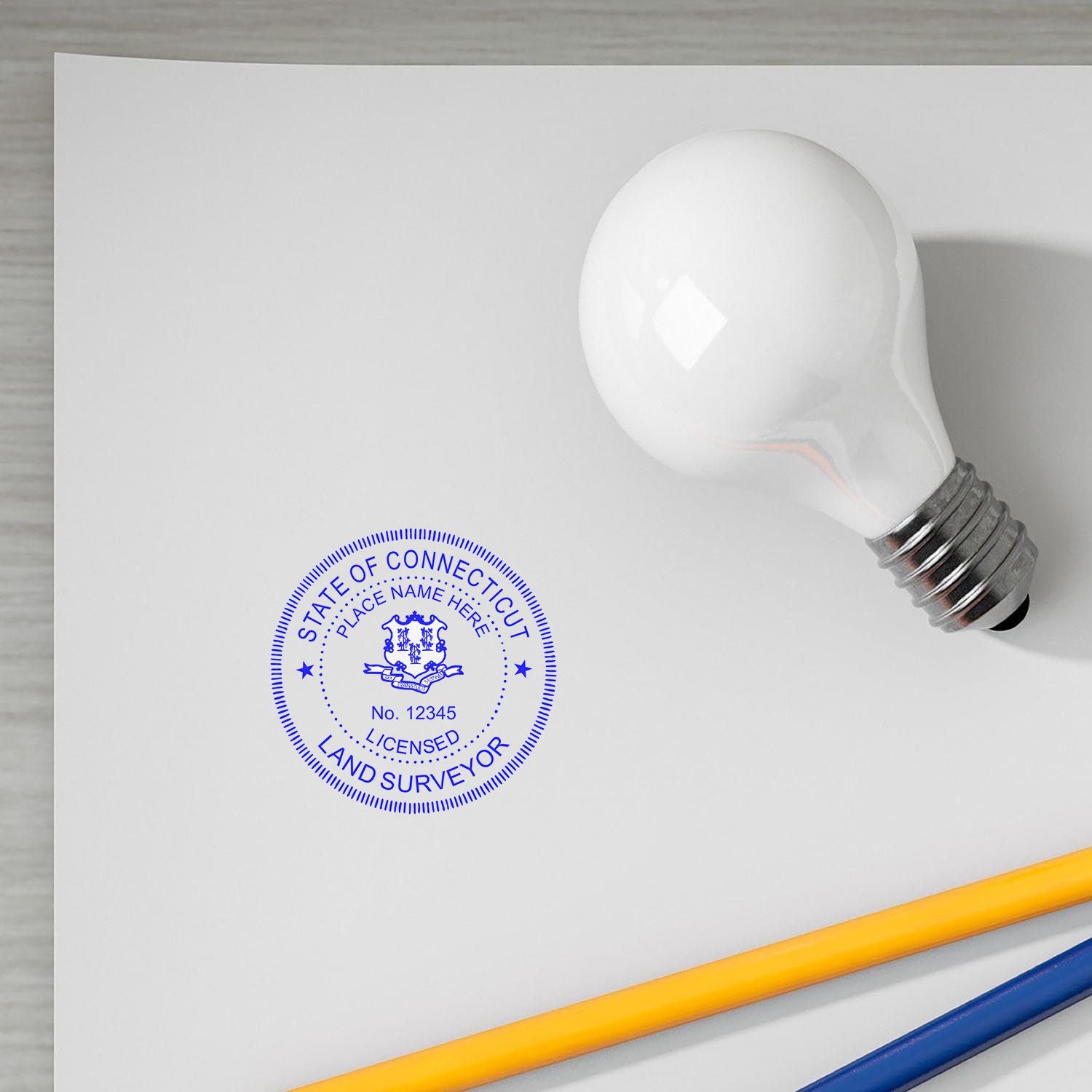 Premium MaxLight Pre-Inked Connecticut Surveyors Stamp on white paper with a light bulb and pencils nearby.