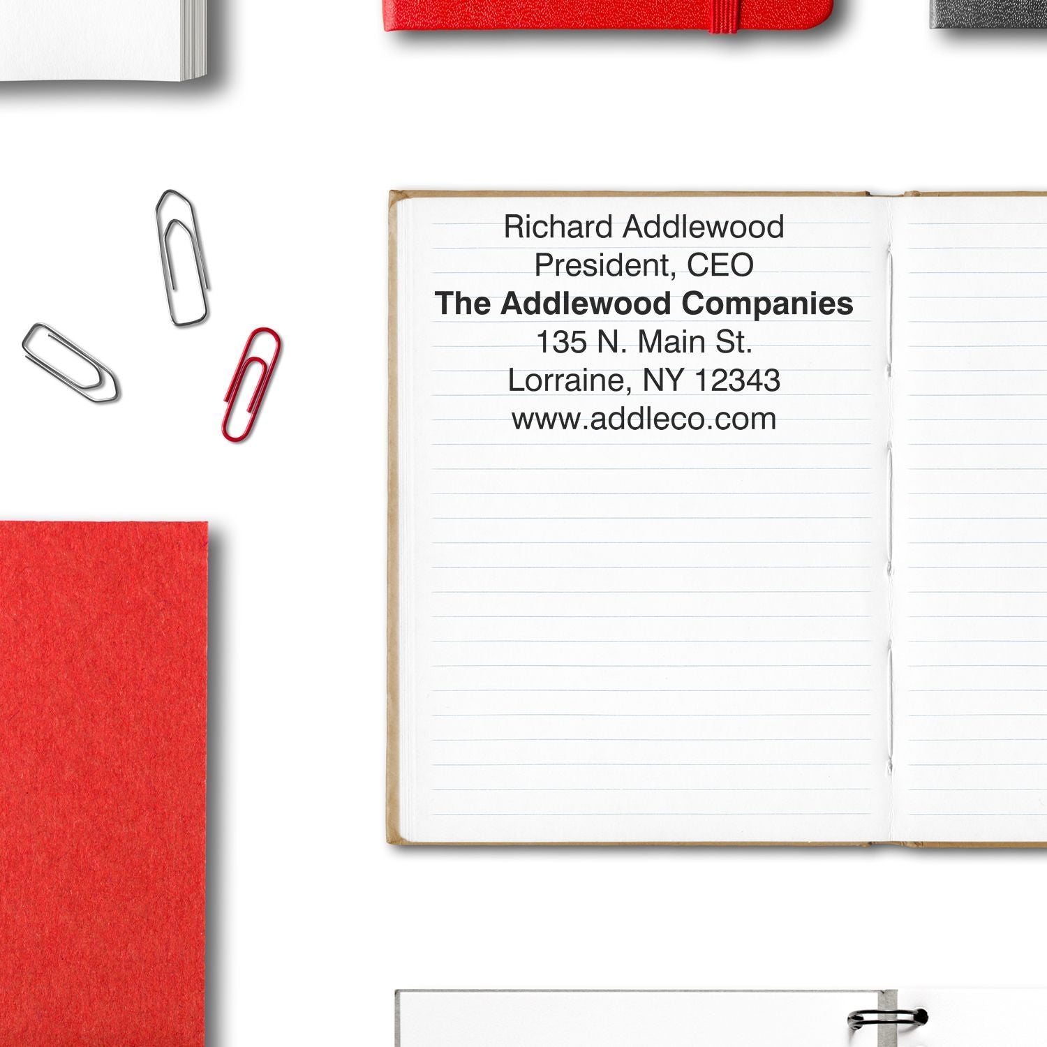 Custom Rubber Stamp Size 5 x 8 used on an open notebook with text, surrounded by paperclips, red and white notebooks, and a binder clip.