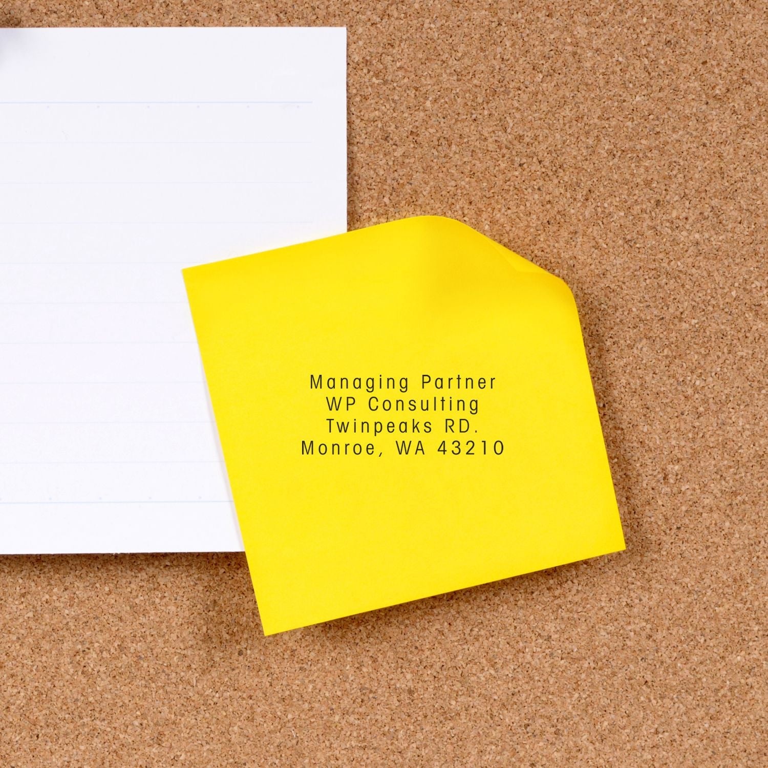 Custom Rubber Stamp Size 1 x 2 used on a yellow sticky note with text Managing Partner, WP Consulting, Twinpeaks RD, Monroe, WA 43210 on a corkboard.