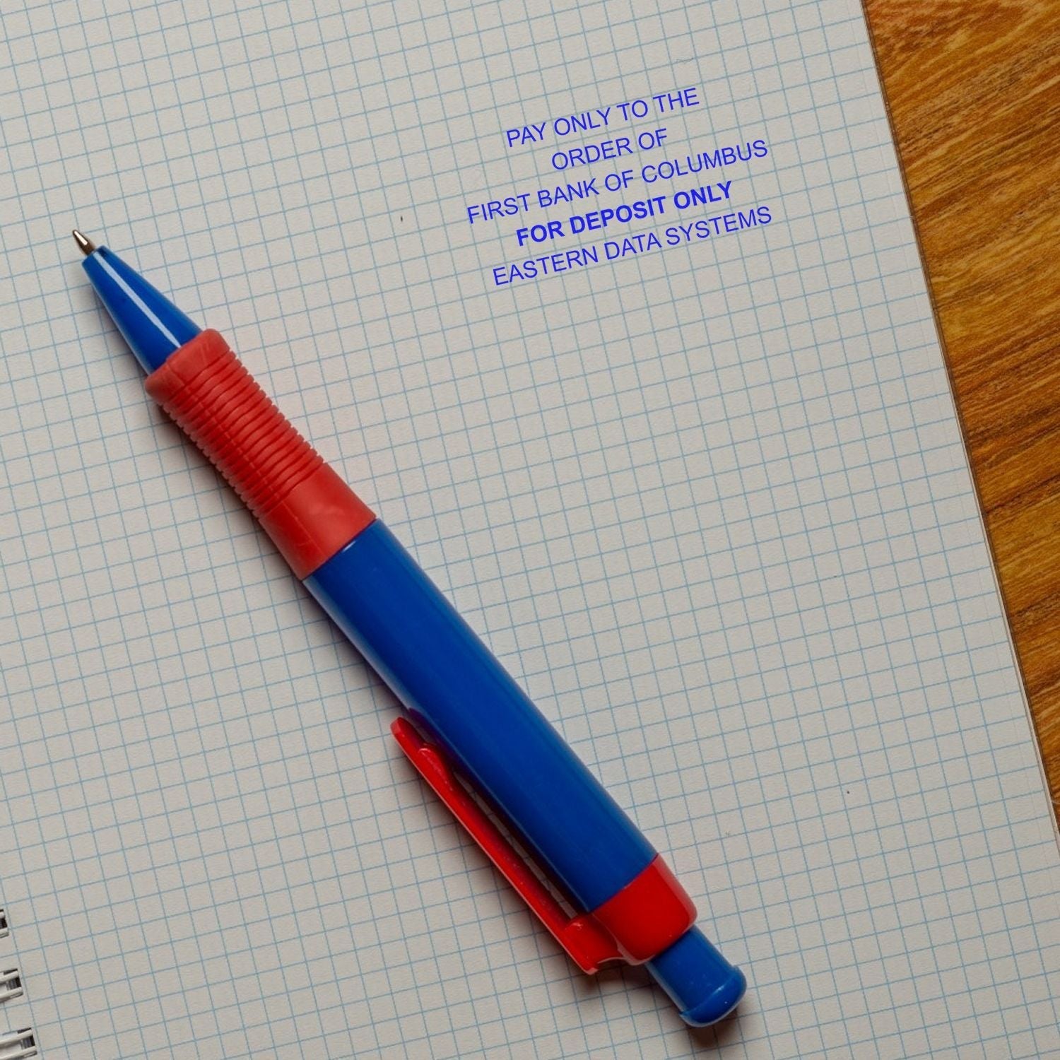 A blue and red pen on graph paper with a stamped message using the MaxLight XL2-165 Custom Pre-Inked Business Stamp 1-1/2 x 2-1/2.