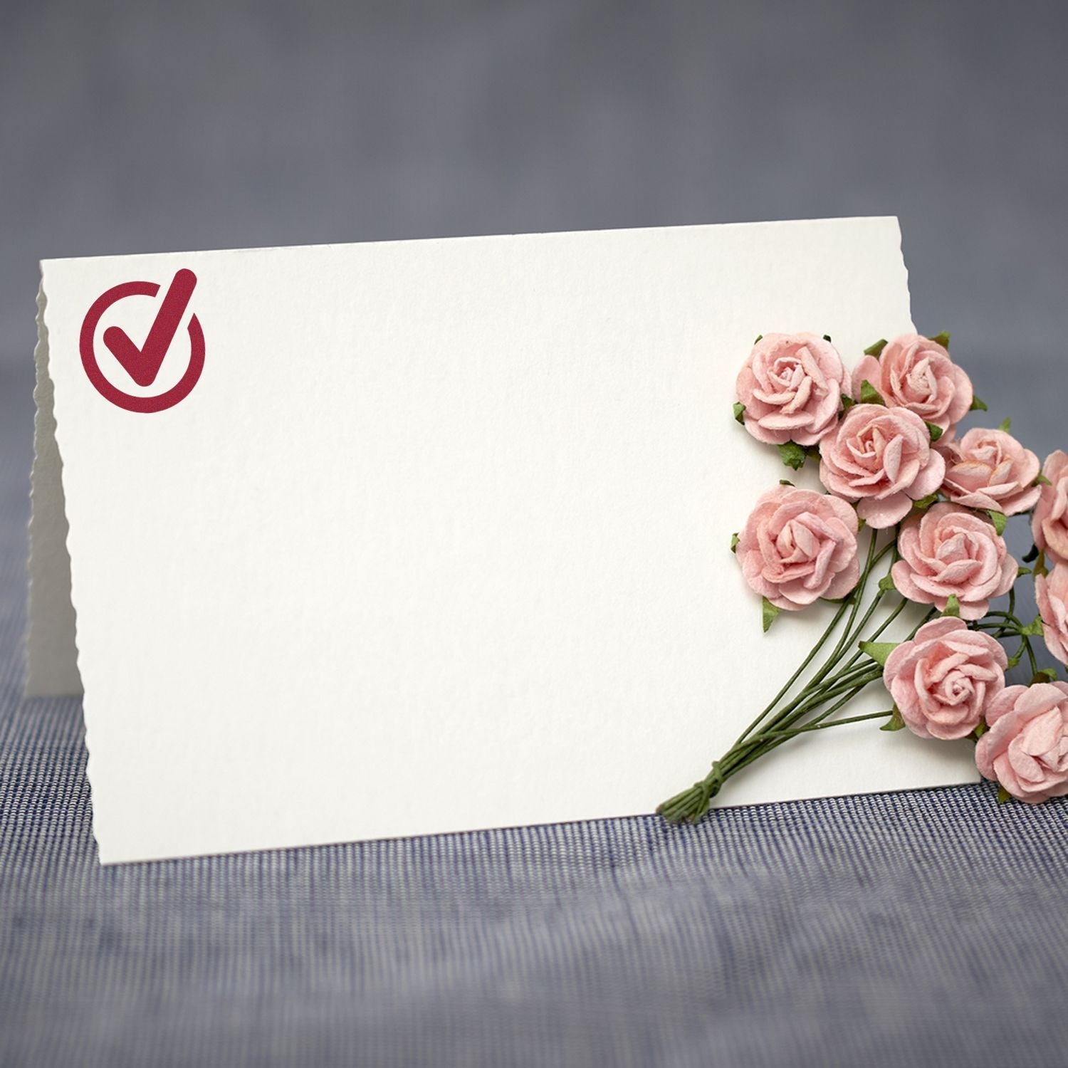 A Custom Rubber Stamp Size 1 Inch Diameter with a checkmark design is stamped on a blank card next to a bouquet of small pink roses.