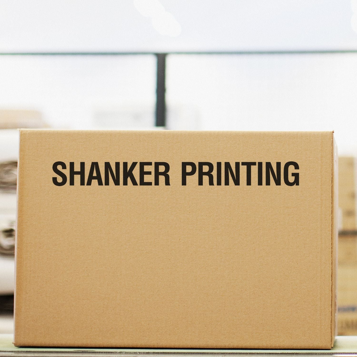 Cardboard box stamped with SHANKER PRINTING using Custom Rubber Stamp Size 1-1/2 x 9, placed in a warehouse setting.