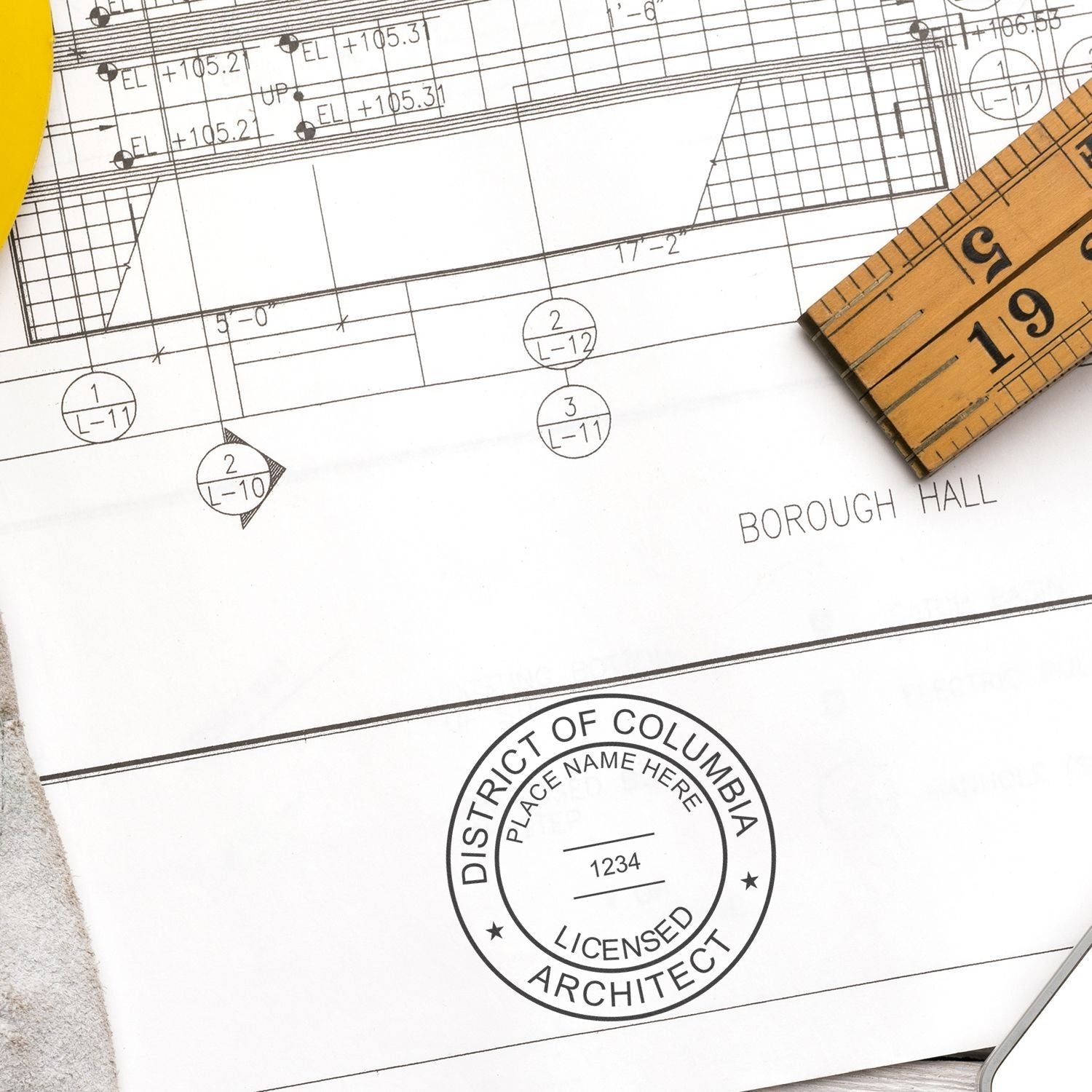 Self Inking District of Columbia Architect Stamp in use on architectural blueprint with a ruler and yellow pen nearby.