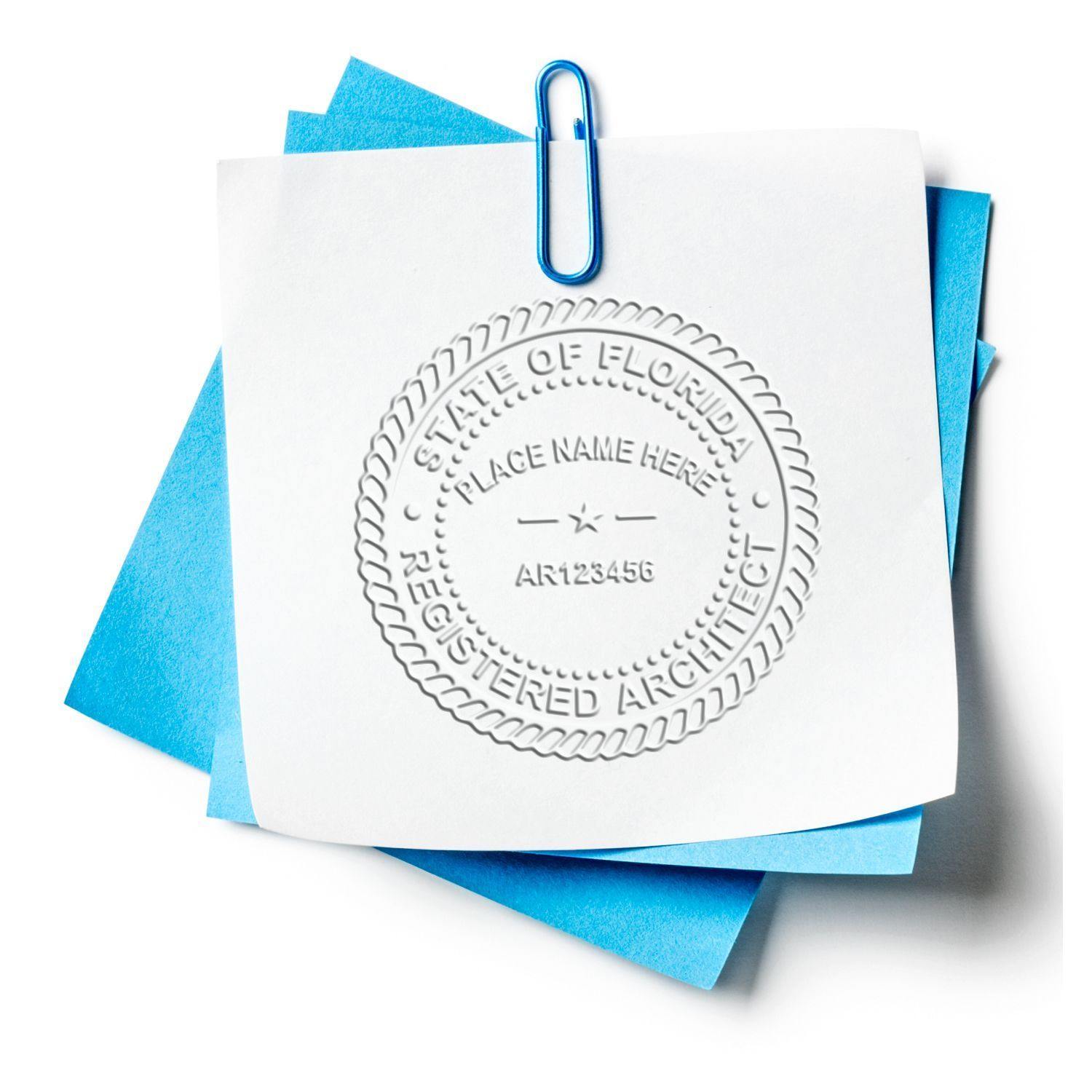 A white paper embossed with a State of Florida Registered Architect seal using the Architect Soft Handheld Seal Embosser, clipped to blue papers with a blue paperclip.