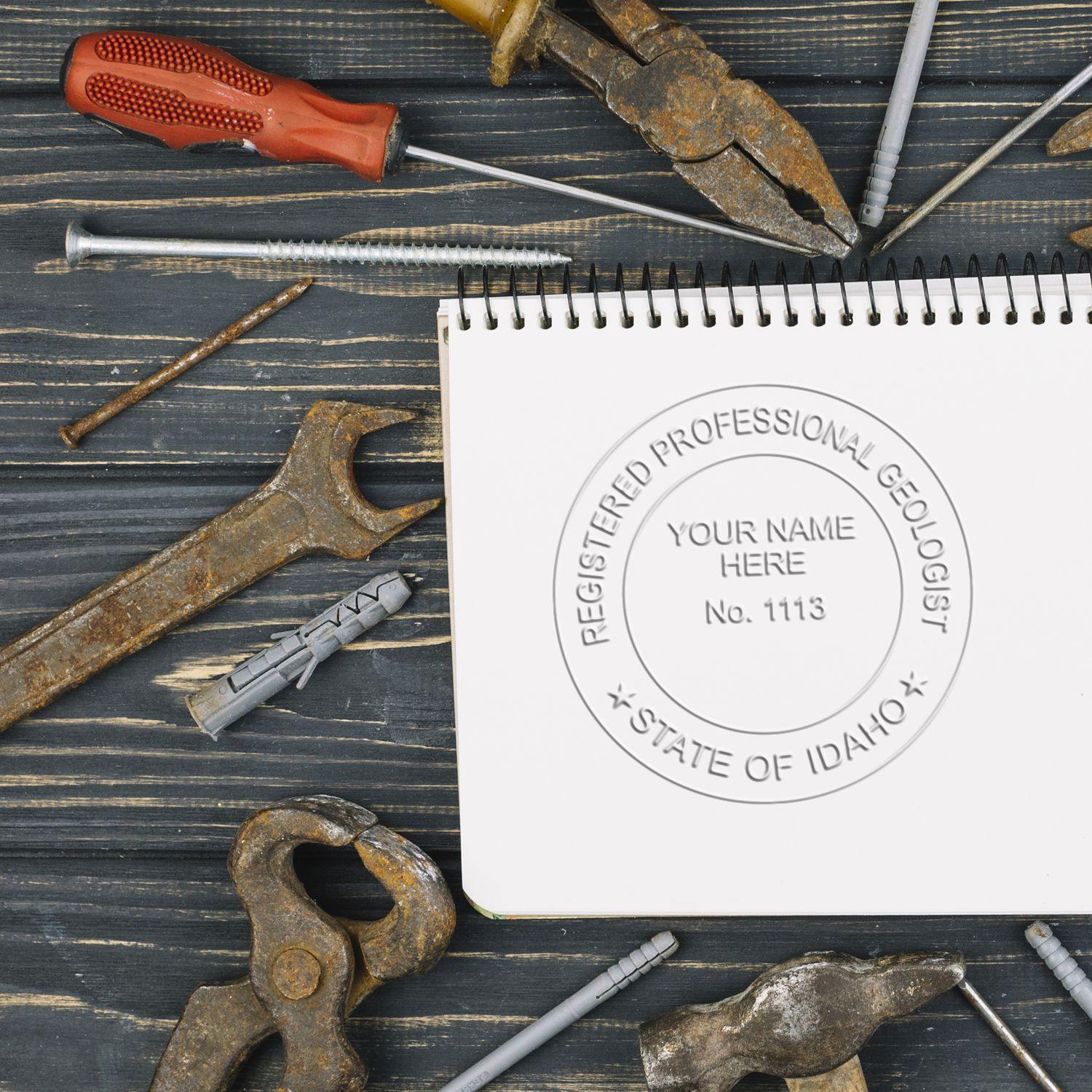 Geologist Hybrid Seal Embosser imprint on a notebook, surrounded by various rusty tools on a wooden surface.