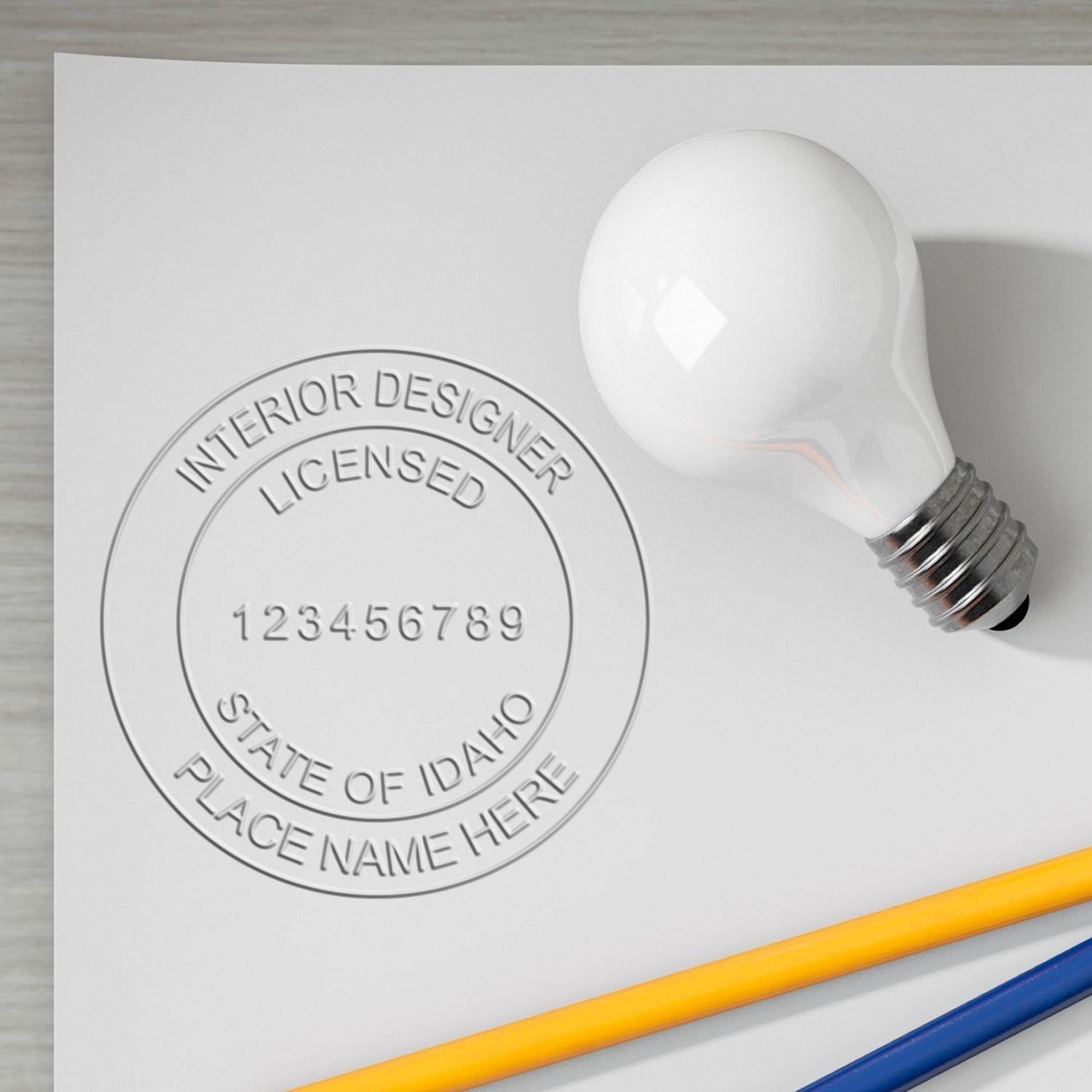 Interior Designer Cast Iron Desk Seal Embosser imprint on paper with a light bulb and colored pencils nearby.