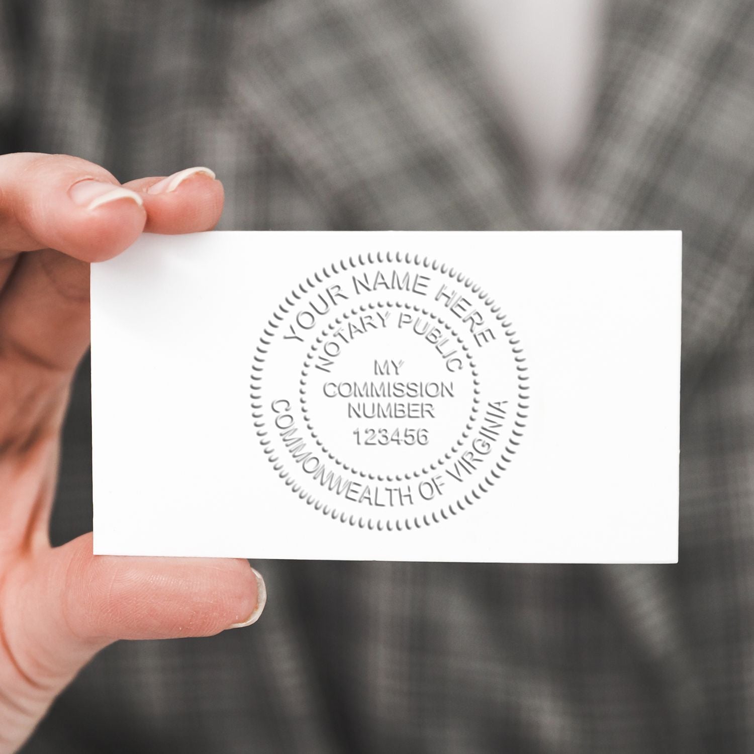 Hand holding a card with an embossed notary seal created by the Pink Hybrid Notary Embosser, displaying Your Name Here and Commonwealth of Virginia.