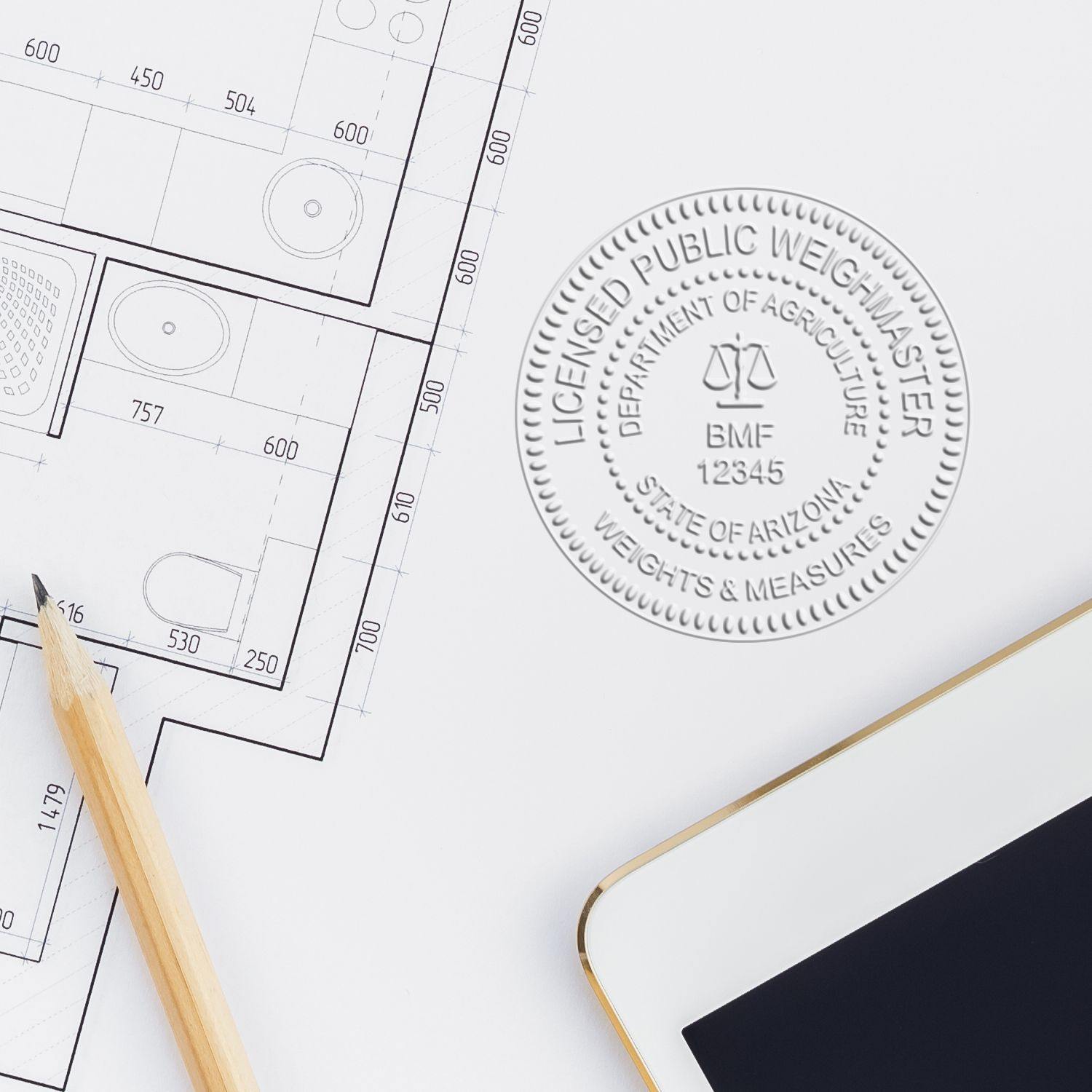 Public Weighmaster Black Gift Seal Embosser imprint on a white paper next to a pencil, architectural plans, and a smartphone.