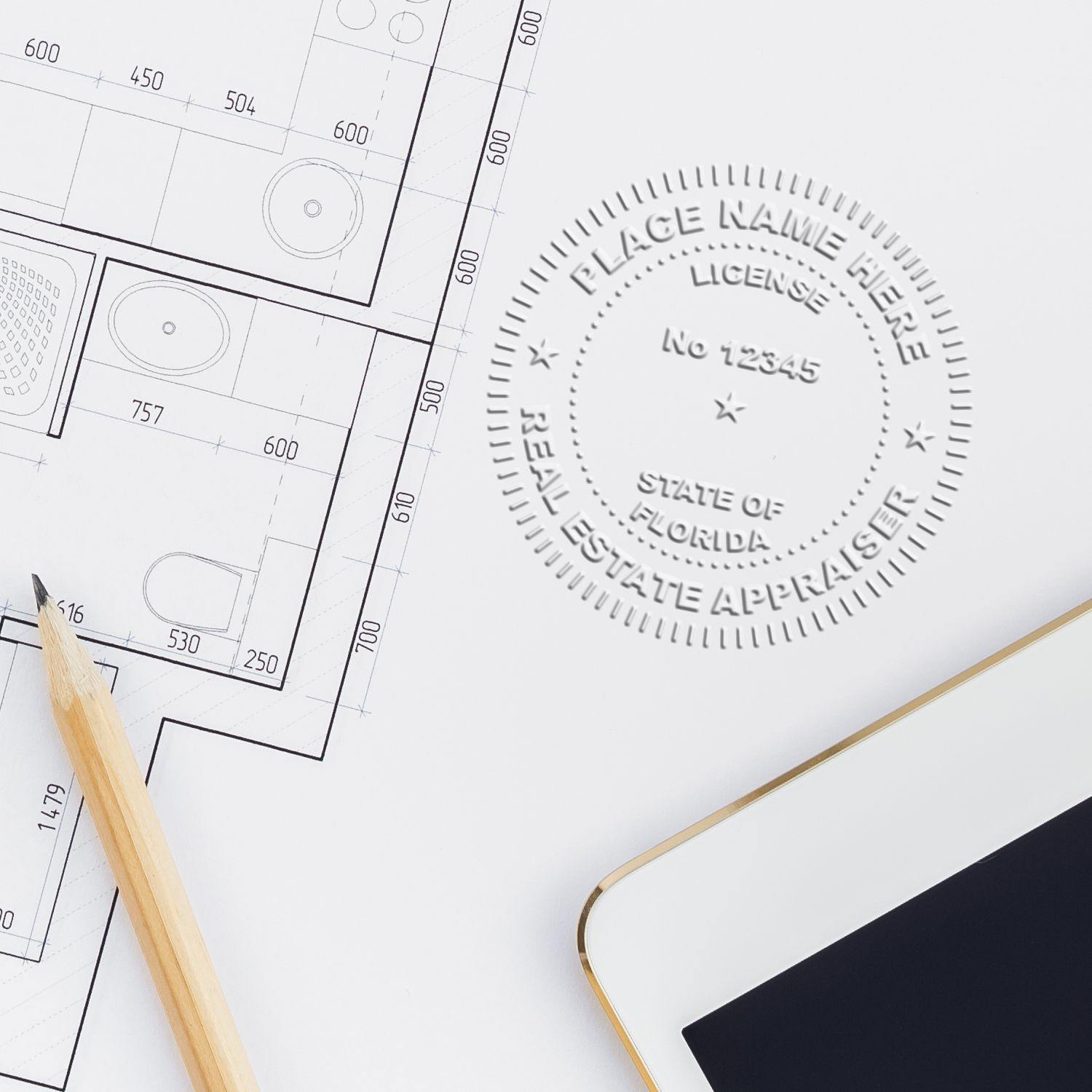 Real Estate Appraiser Hybrid Seal Embosser in use on architectural plans, with a pencil and tablet nearby.