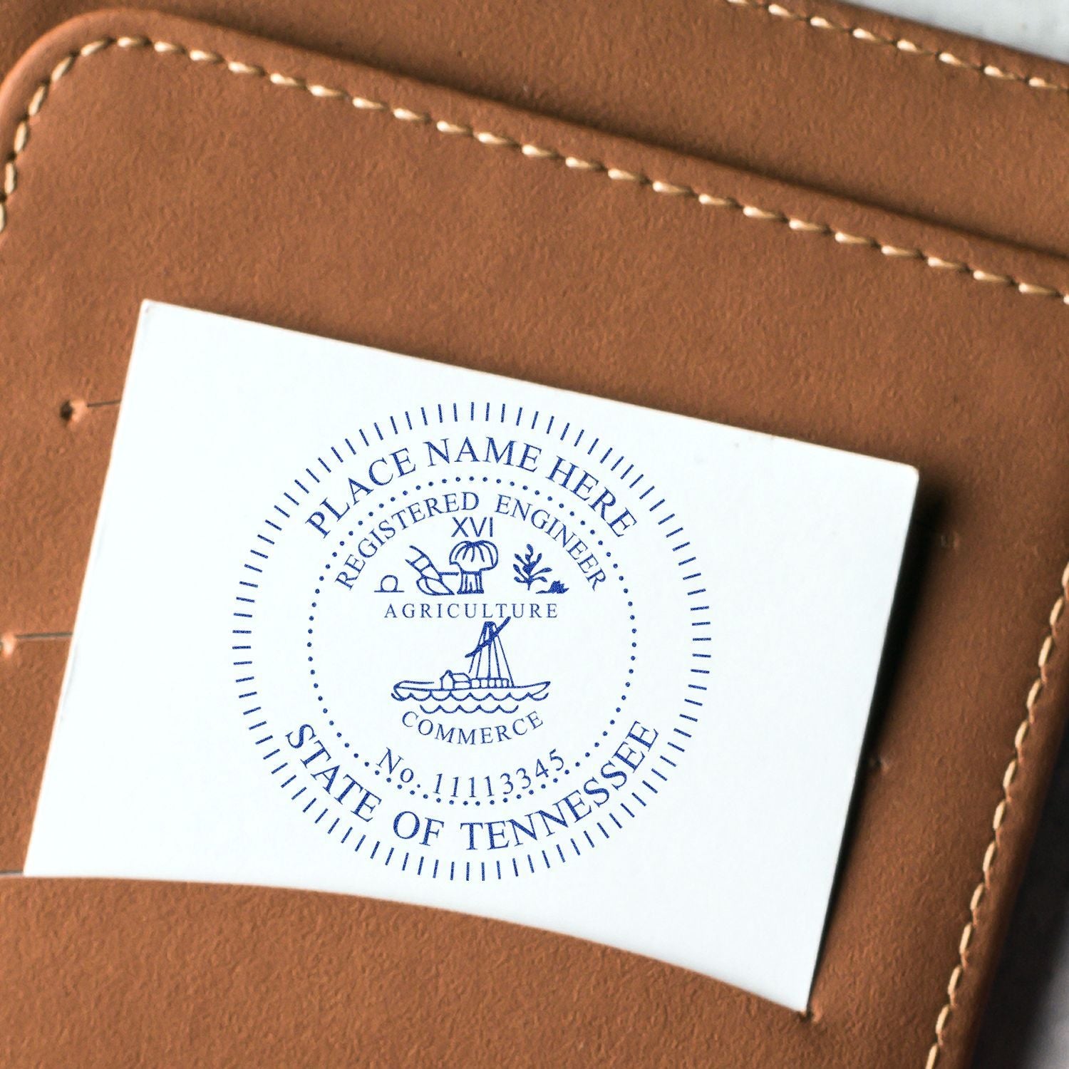 A close-up of a white card stamped with the Professional Engineer Regular Rubber Stamp of Seal, featuring a detailed circular design with text and symbols, placed on a brown leather surface.