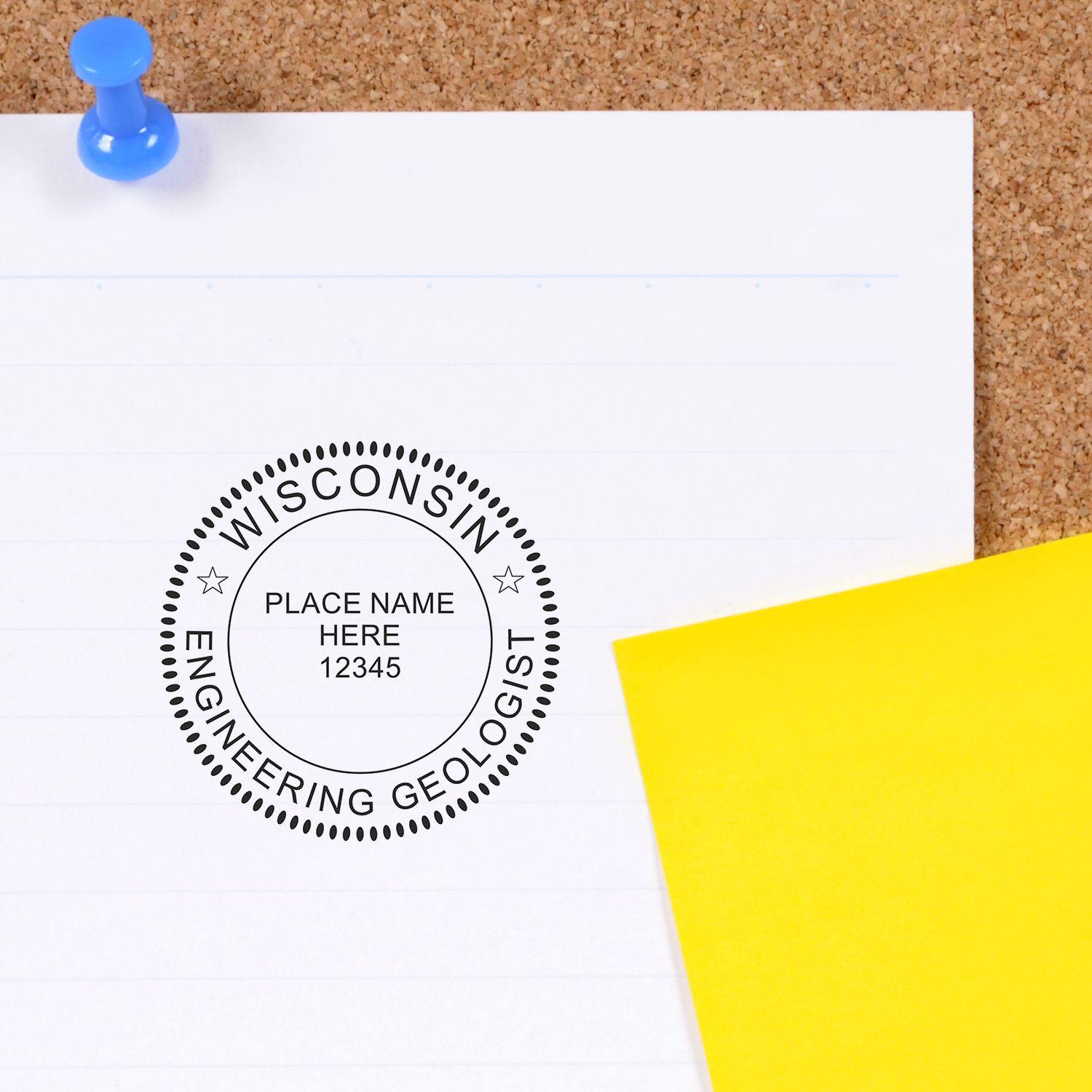 A white sheet of paper stamped with the Engineering Geologist Regular Rubber Stamp of Seal, displaying Wisconsin Engineering Geologist with a placeholder for name and number, next to a yellow sticky note on a corkboard.