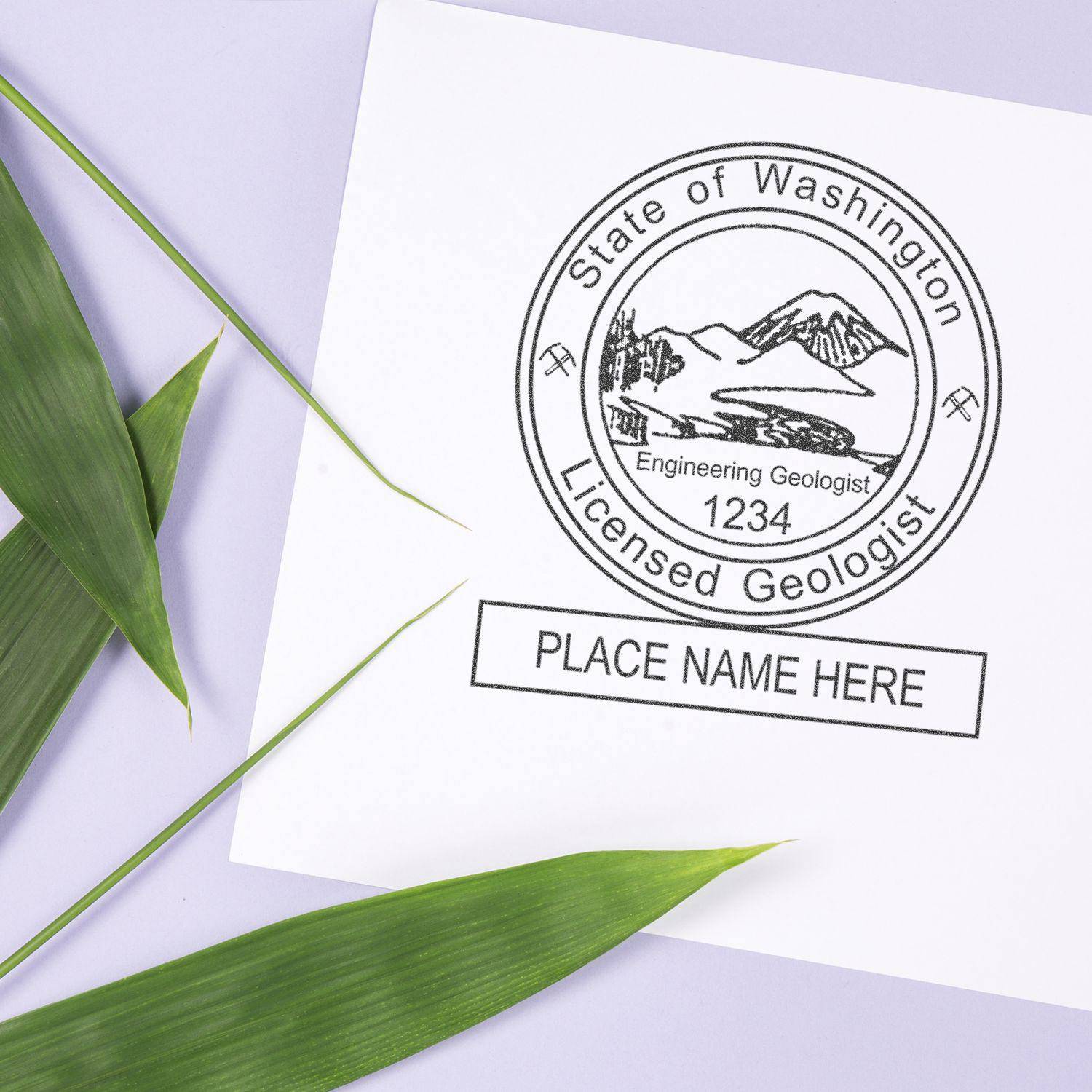 Engineering Geologist Regular Rubber Stamp of Seal on white paper with green leaves. The stamp shows State of Washington Licensed Geologist with a mountain design and space for a name and number.